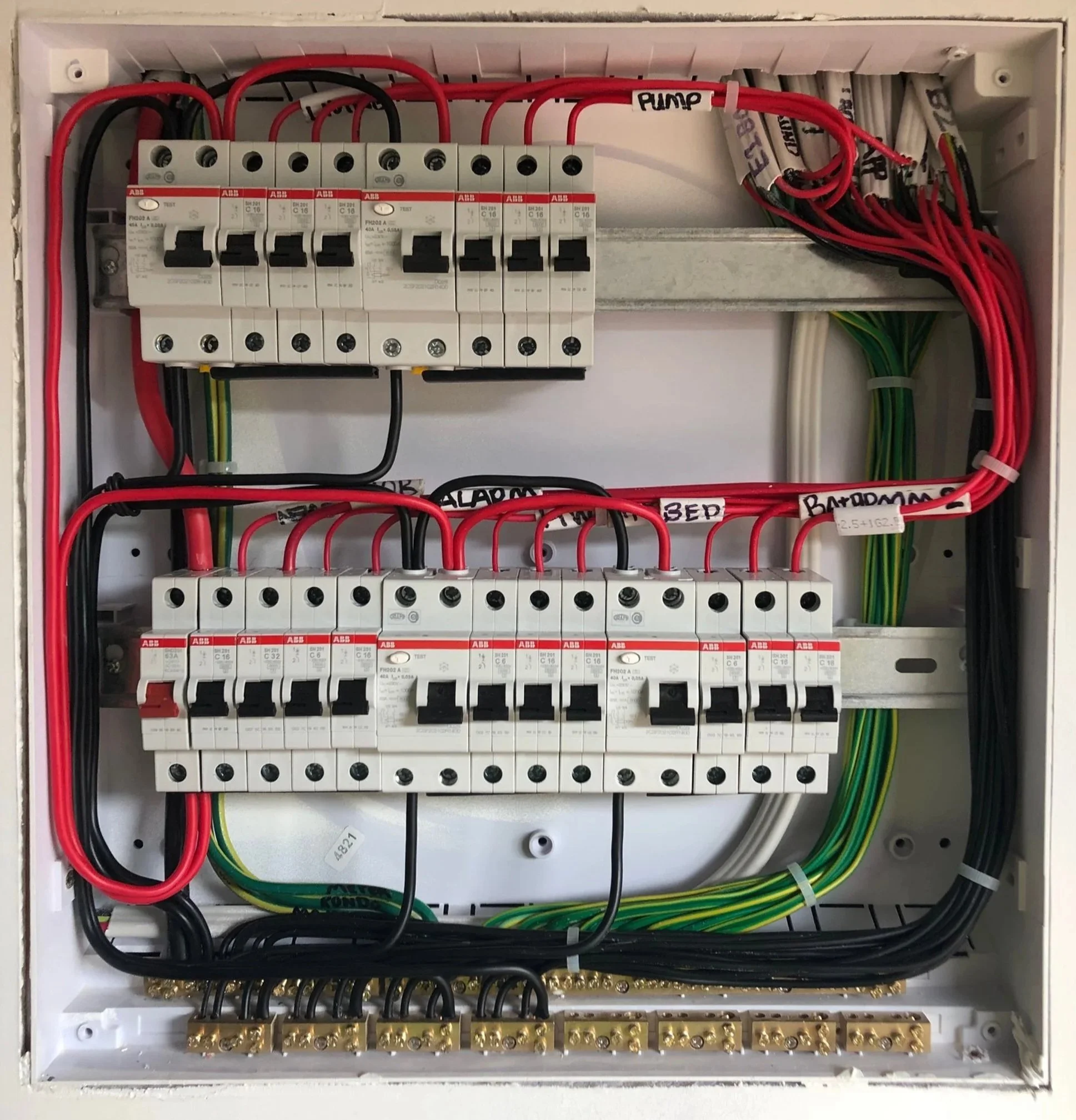 Electrical breaker box with circuit breakers labeled for various systems such as alarm, HVAC, and bedrooms, with organized wiring and labeled connections.