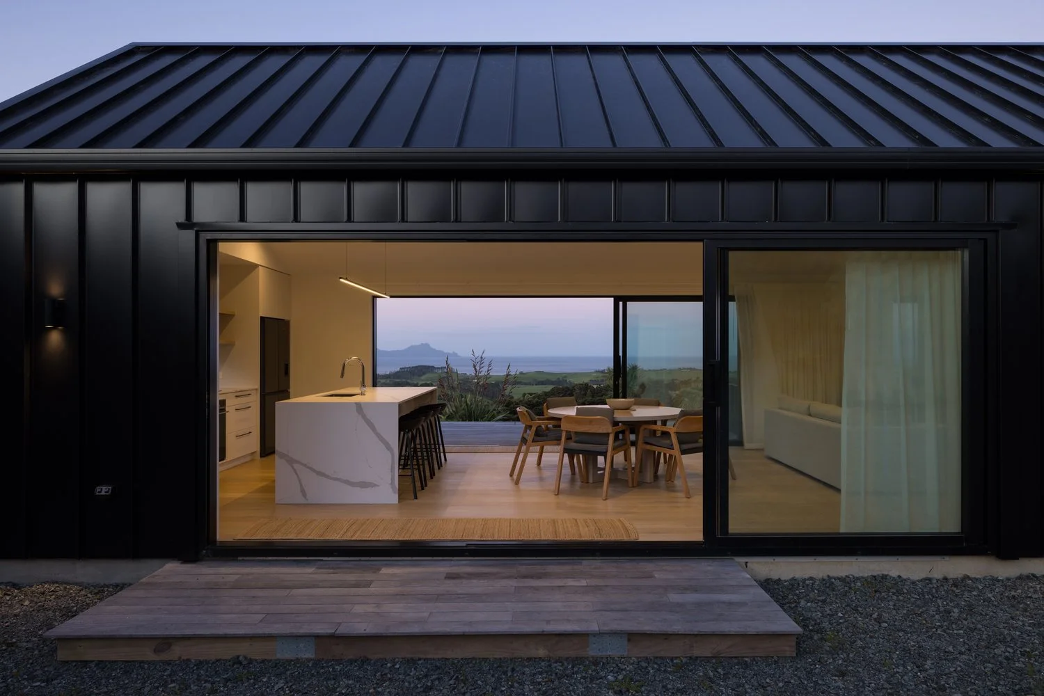 Modern black house with large sliding glass doors revealing a kitchen and dining area with ocean view
