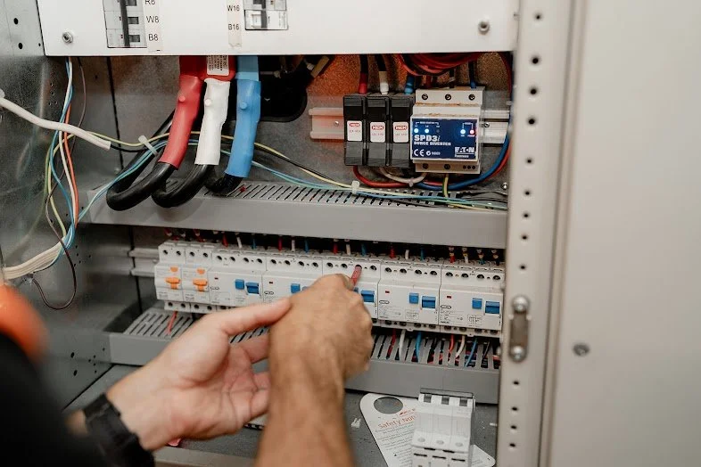 Person working on an electrical panel with circuit breakers and wiring.