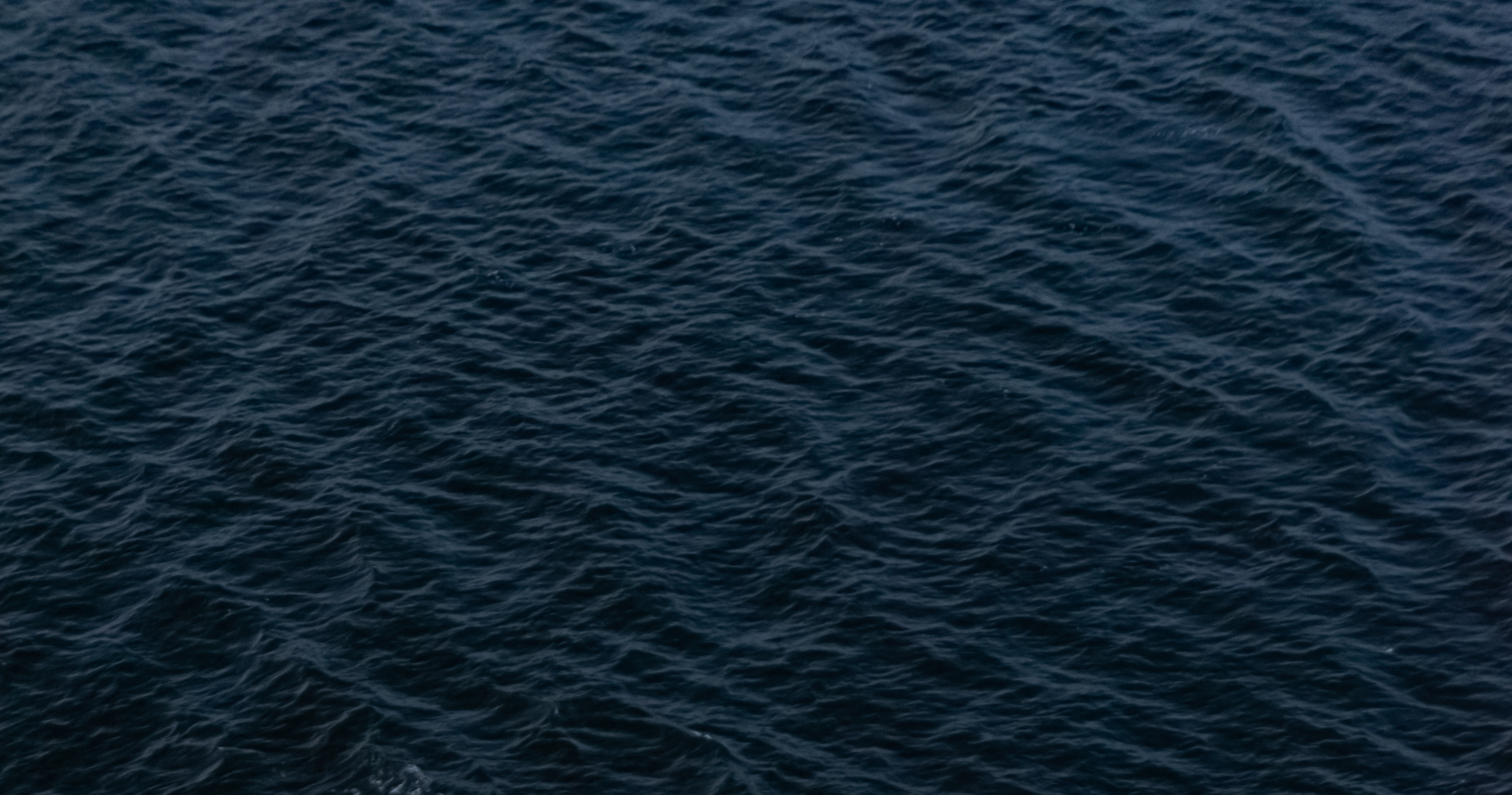 A vast expanse of deep blue ocean water with visible waves and ripples.