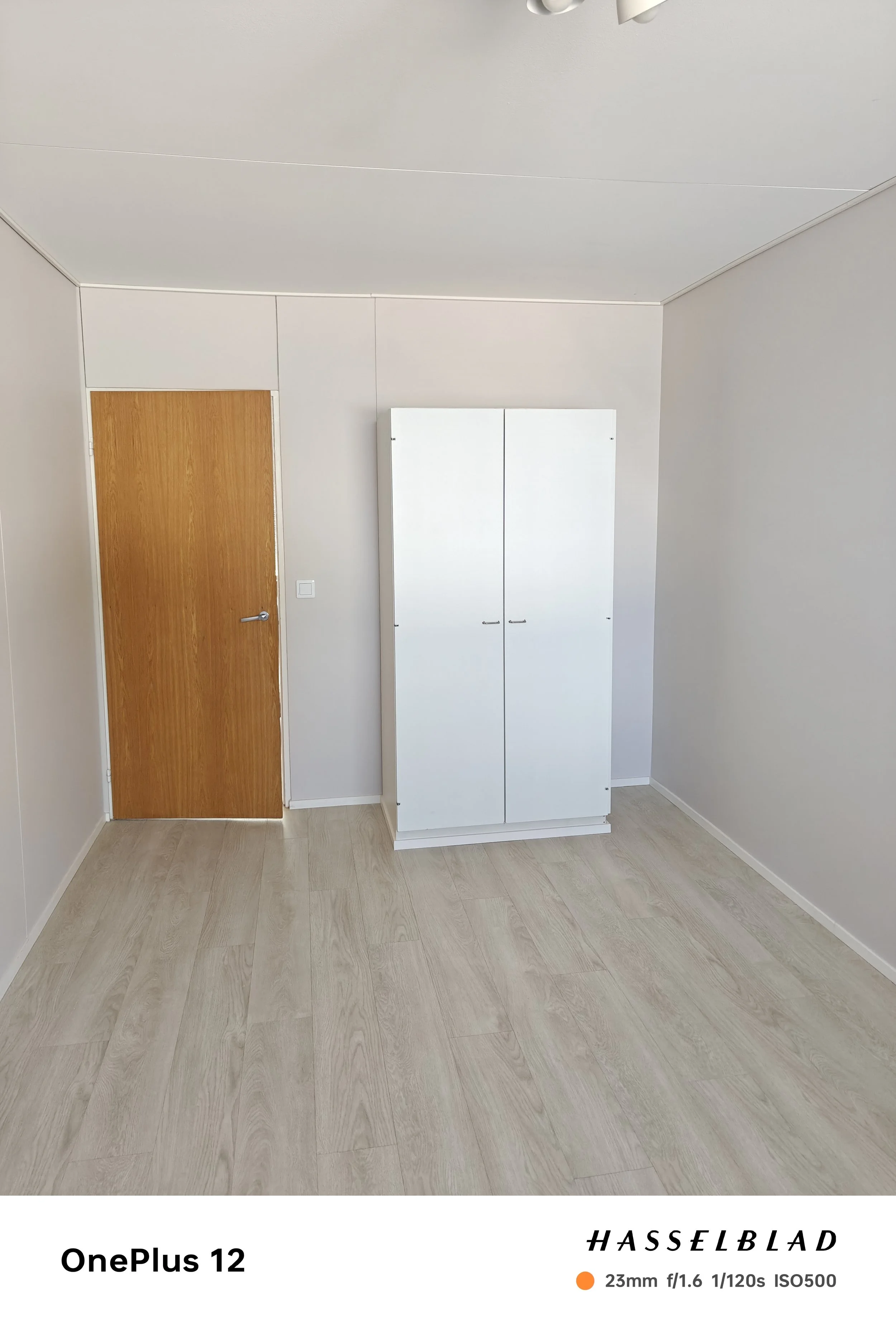 Tyhjä huone, valkoinen kaappi, puinen ovi, puiset lattiat.