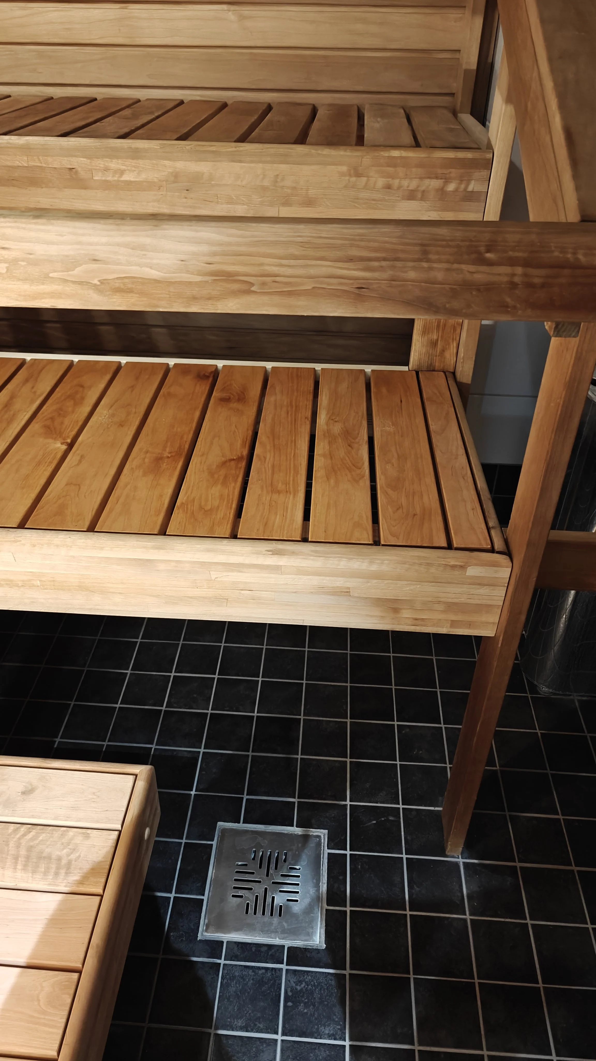 Kuva puisista saunan lauteista ja lattianristiästä kylpyhuoneessa.