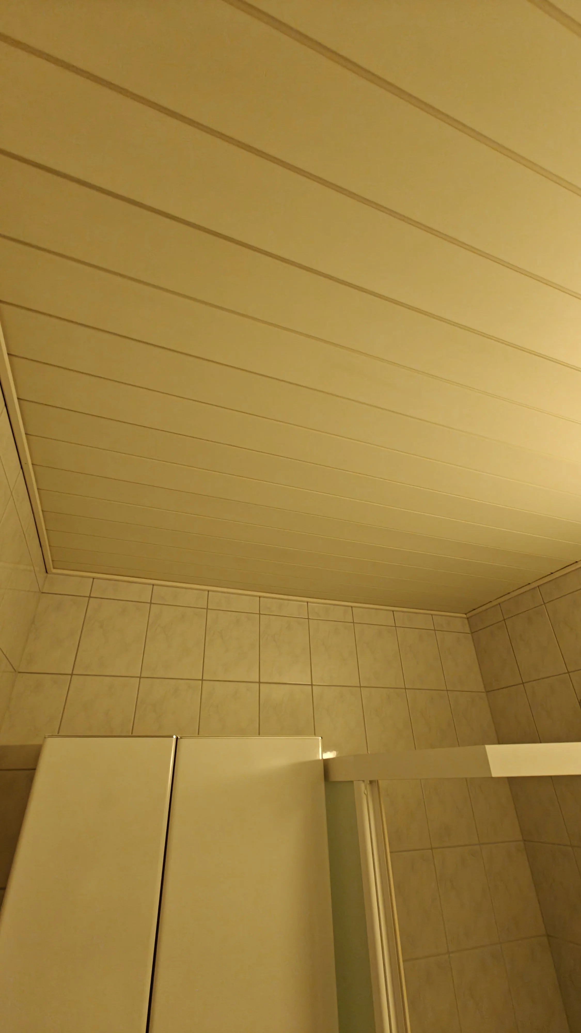 Kuva suihkuhuoneen katosta ja seinistä, joissa on vaaleat laatat ja keltainen katto.