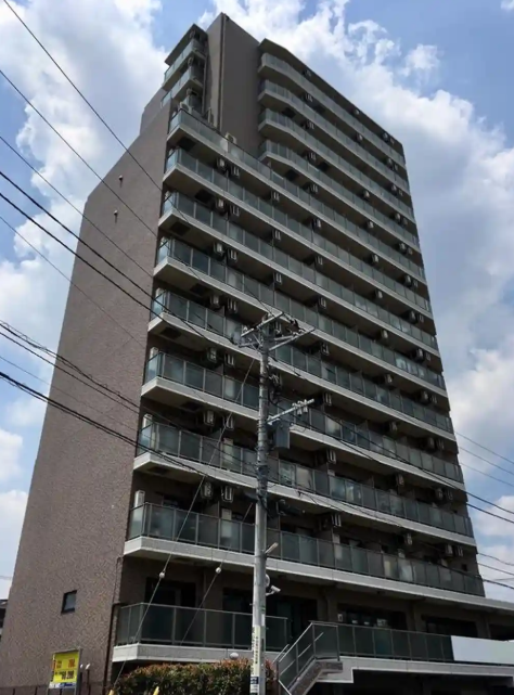 高層のマンションの建物と、その前にある電柱と電線。青空と雲が見える風景。