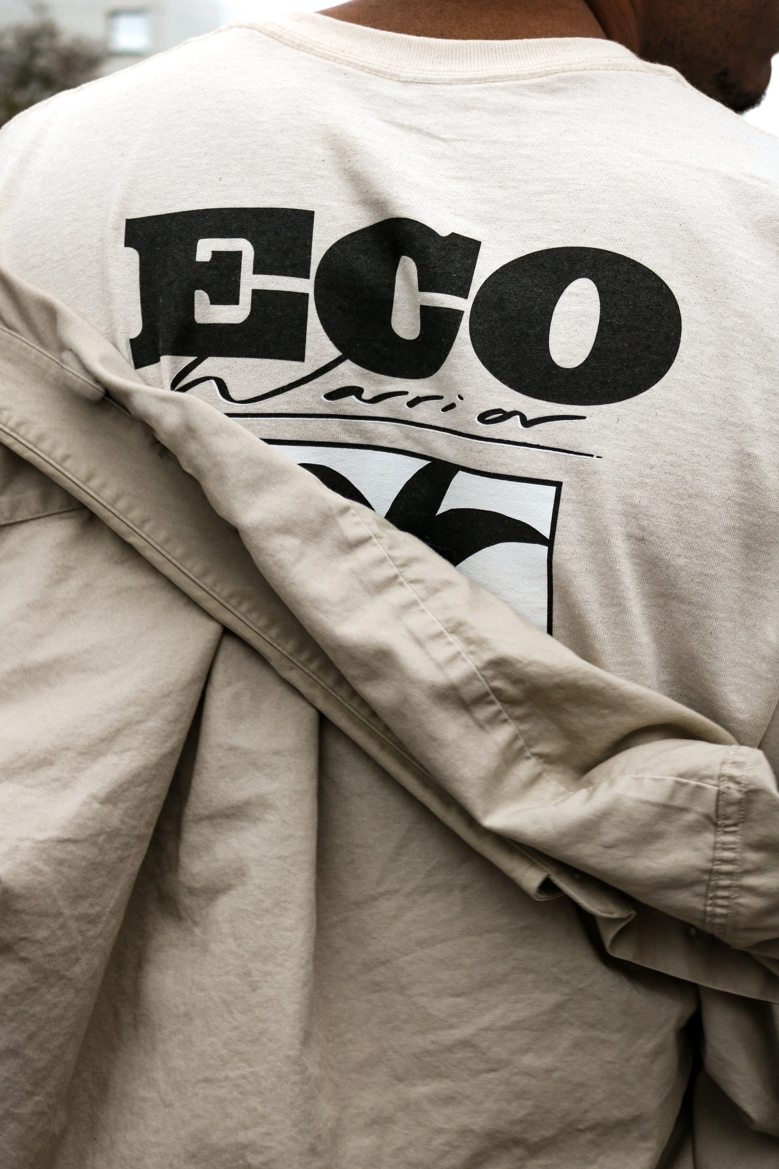 Person wearing a beige jacket over a gray sweatshirt with the text 'ECO' and the number '76' printed on the back.