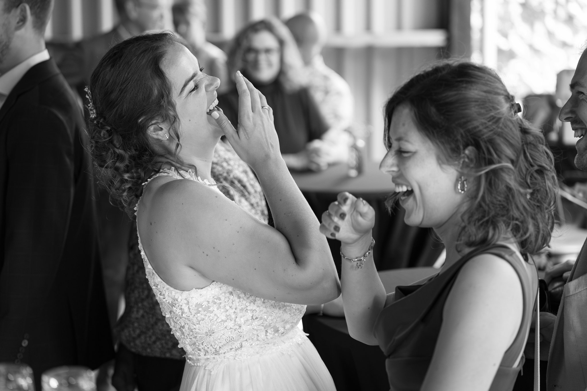 Vreugdevolle vrouwen die lachen en elkaar aanraken op een bruiloft.