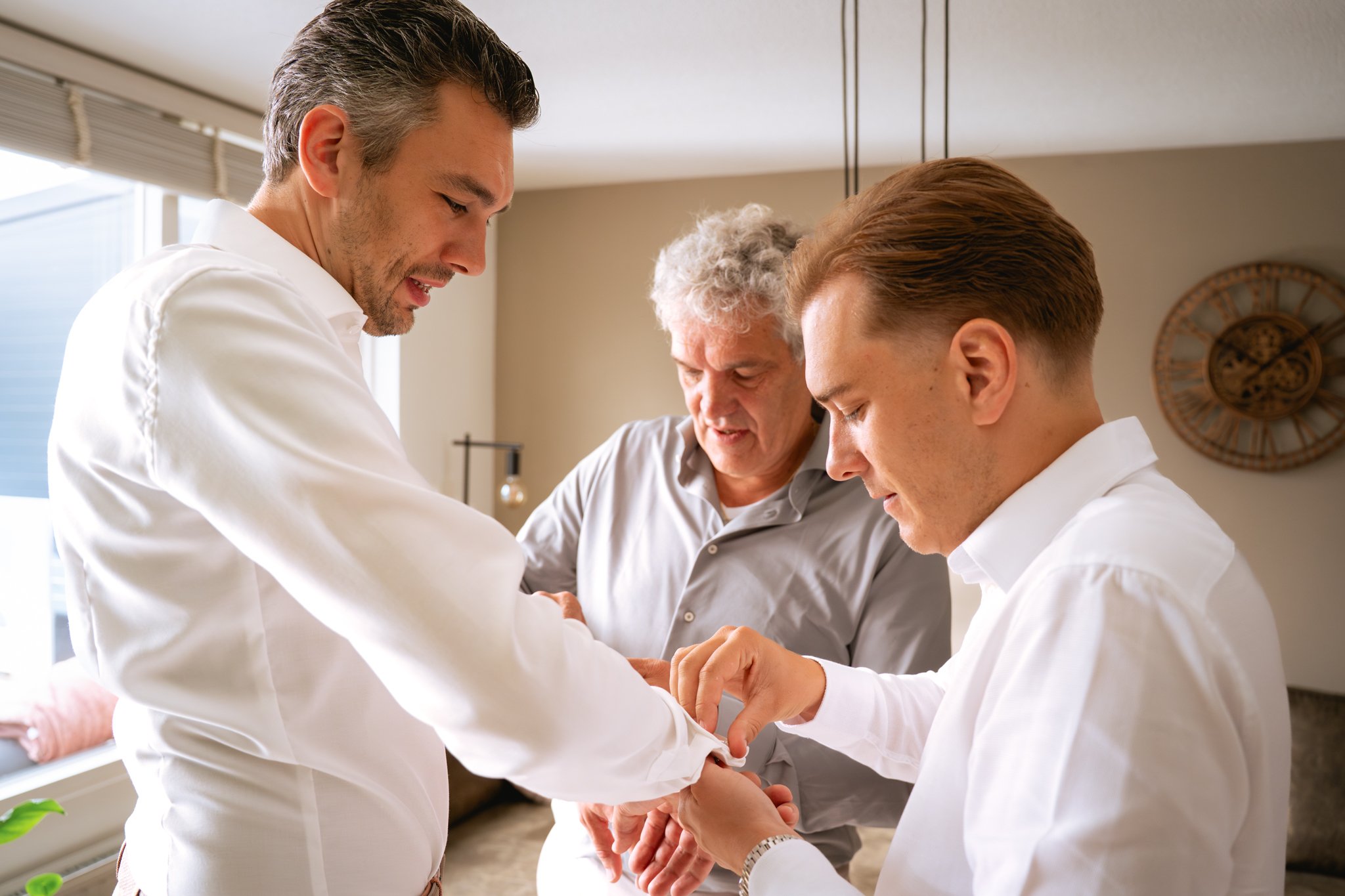twee mannen helpen de bruidegom met het aankleden van zijn pak voor de bruiloft