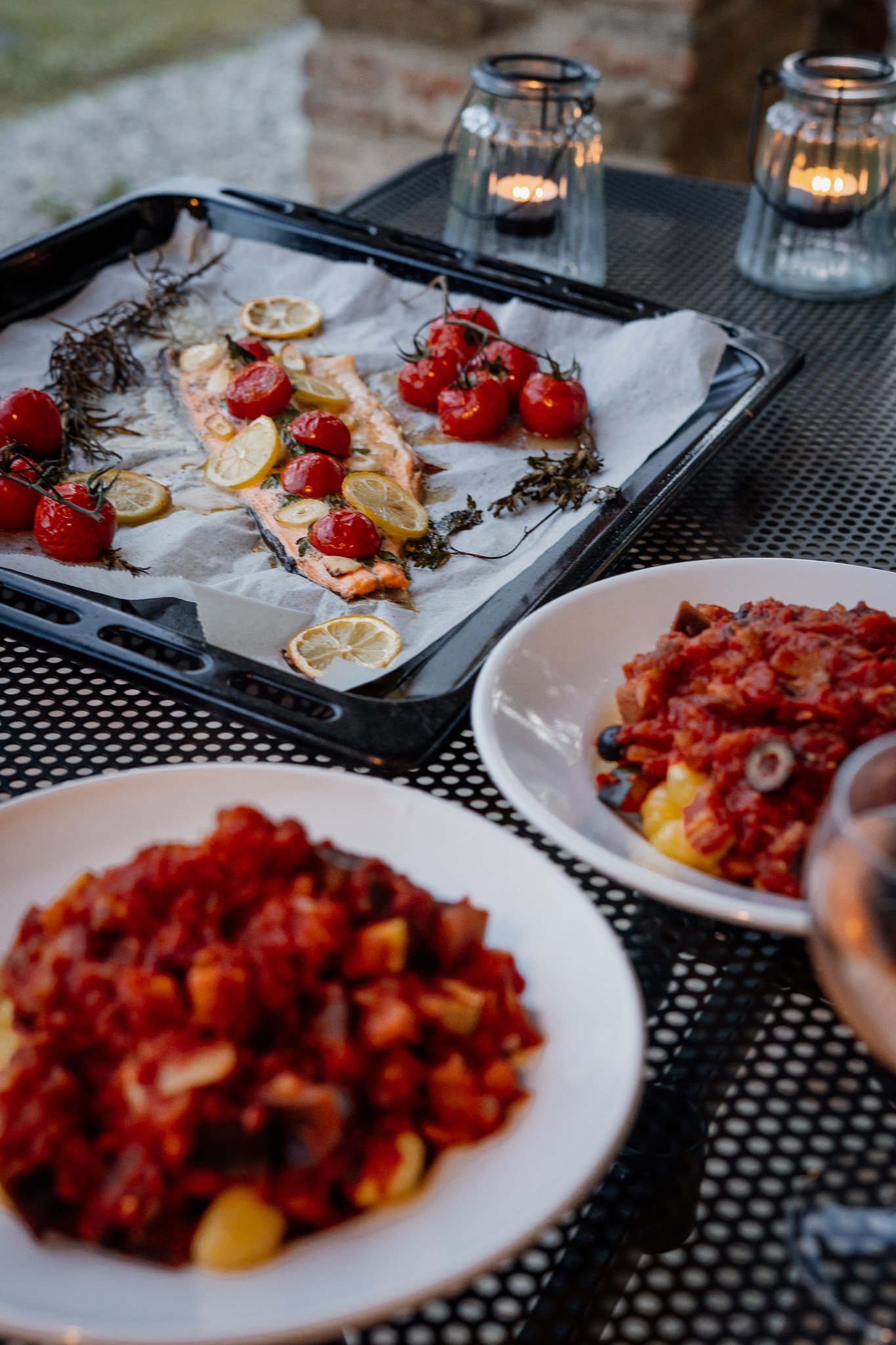 Dinertafel met geroosterde vis met citroen en kersentomaten, en pastagerechten met tomatensaus.