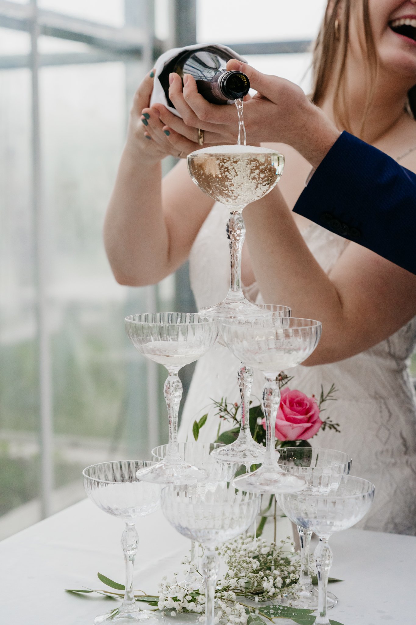 Mensen schenken champagne in een glazen piramide tijdens een celebratie, een huwelijk, met bloemen op de tafel.