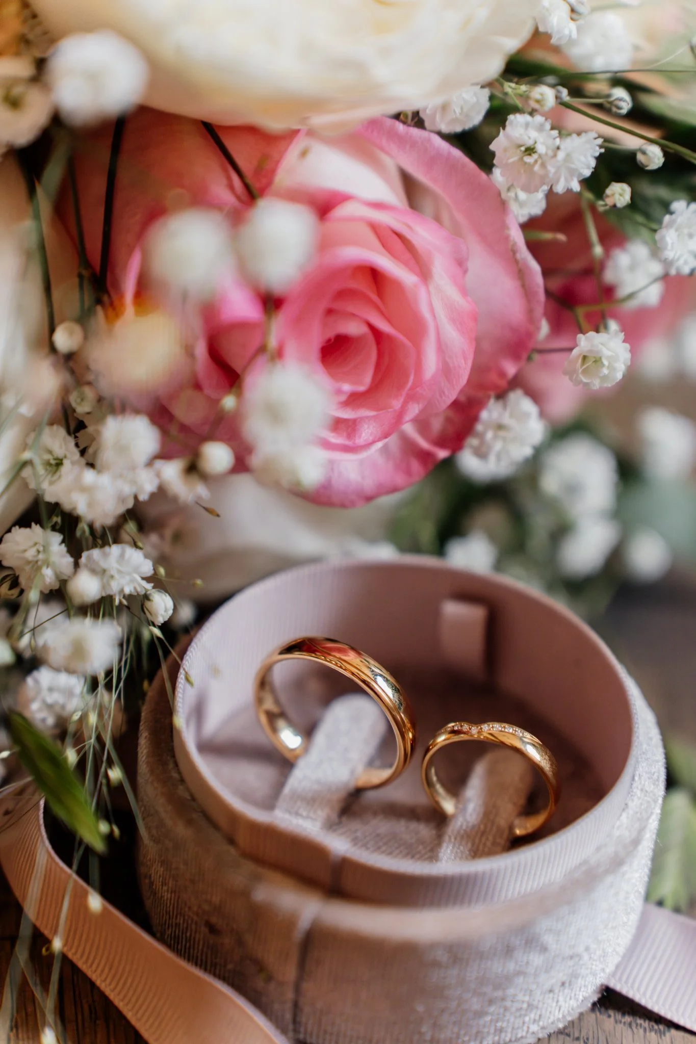 detailfoto van trouwringen in een sieradendoosje, omgeven door een bloemenboeket met roze en witte bloemen.
