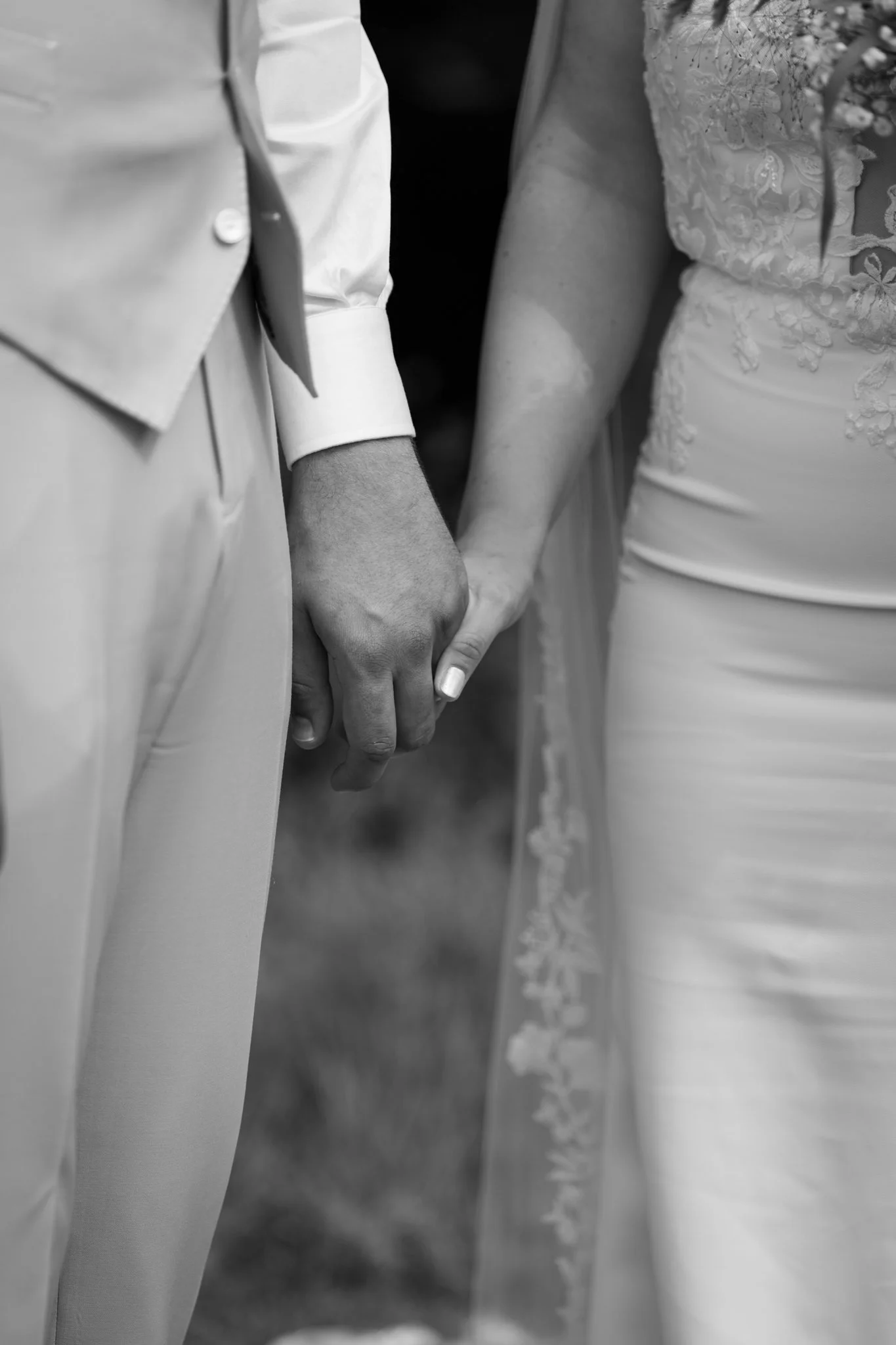 Een close-up van een hand in een trouwjurk die wordt vastgehouden door een hand in een pak, op een huwelijksceremonie.