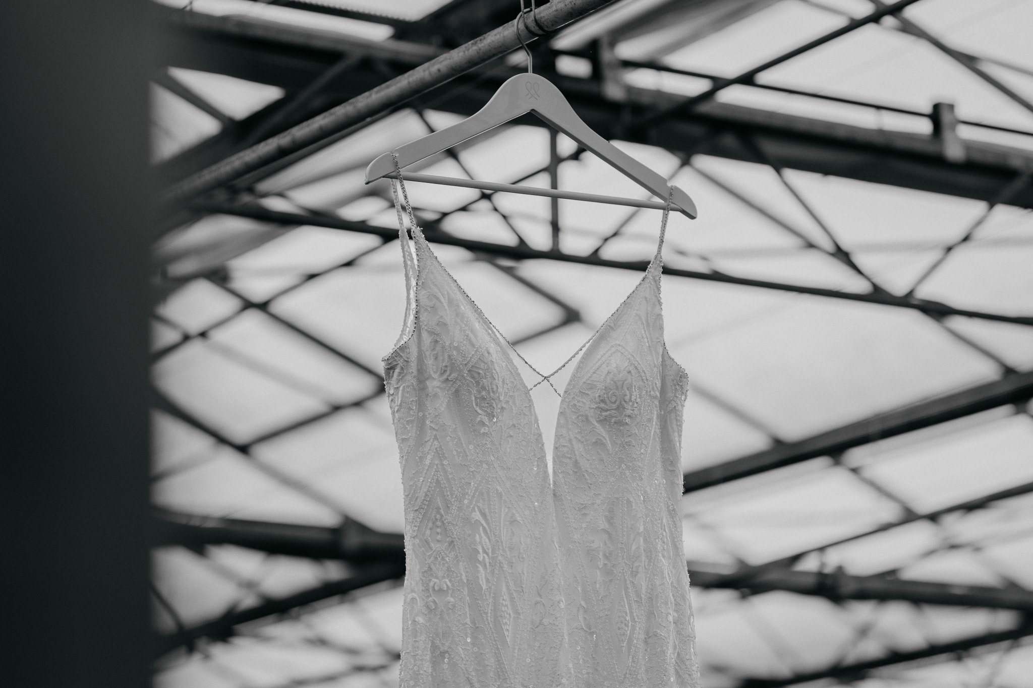 Zweedse kanten trouwjurk hangt aan een witte kledinghanger onder een metalen constructie met een glazen dak.