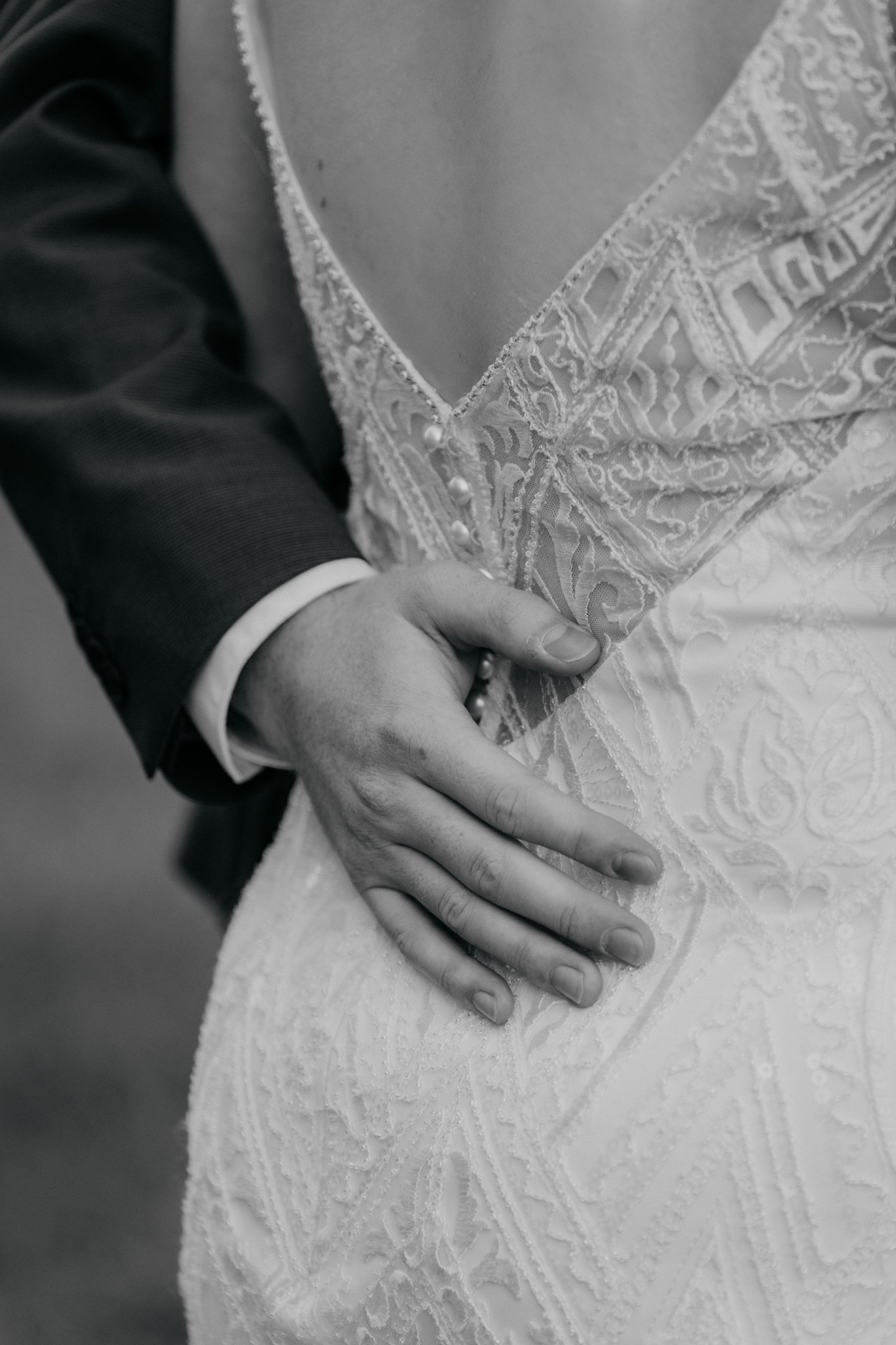 Close-up van een hand die op de taille van een bruidsjurk ligt, zwart-wit foto.