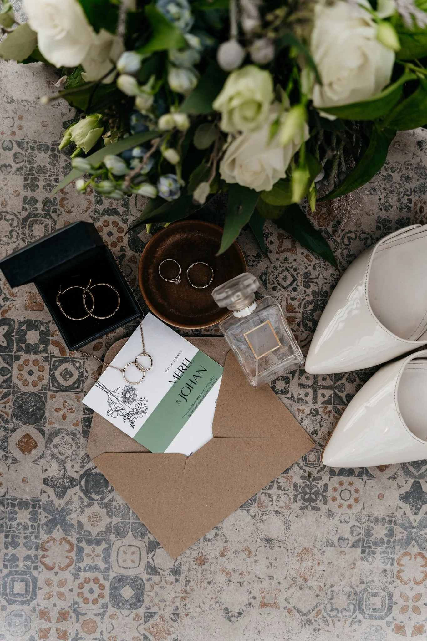 Een detailfoto bij een bruiloft van sieraden, bloemen, een fles parfum en cadeaudozen op een grafiekachtige vloer
