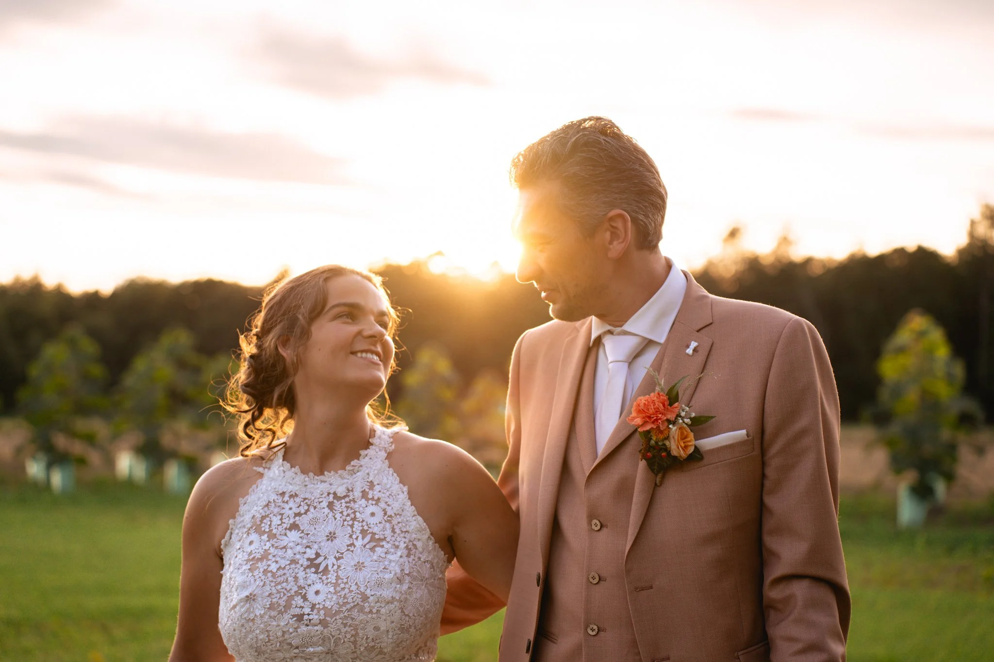 Een bruid en bruidegom kijken elkaar liefdevol aan tijdens hun bruiloft in de buitenlucht bij zonsondergang.