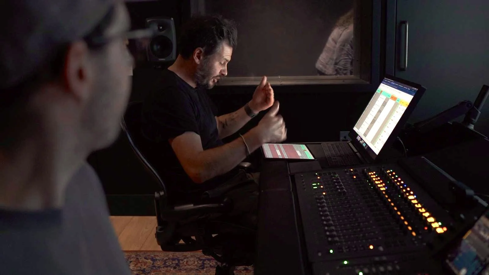 Two men in a recording studio, one using audio mixing equipment and the other observing, with computer screens displaying audio waves.