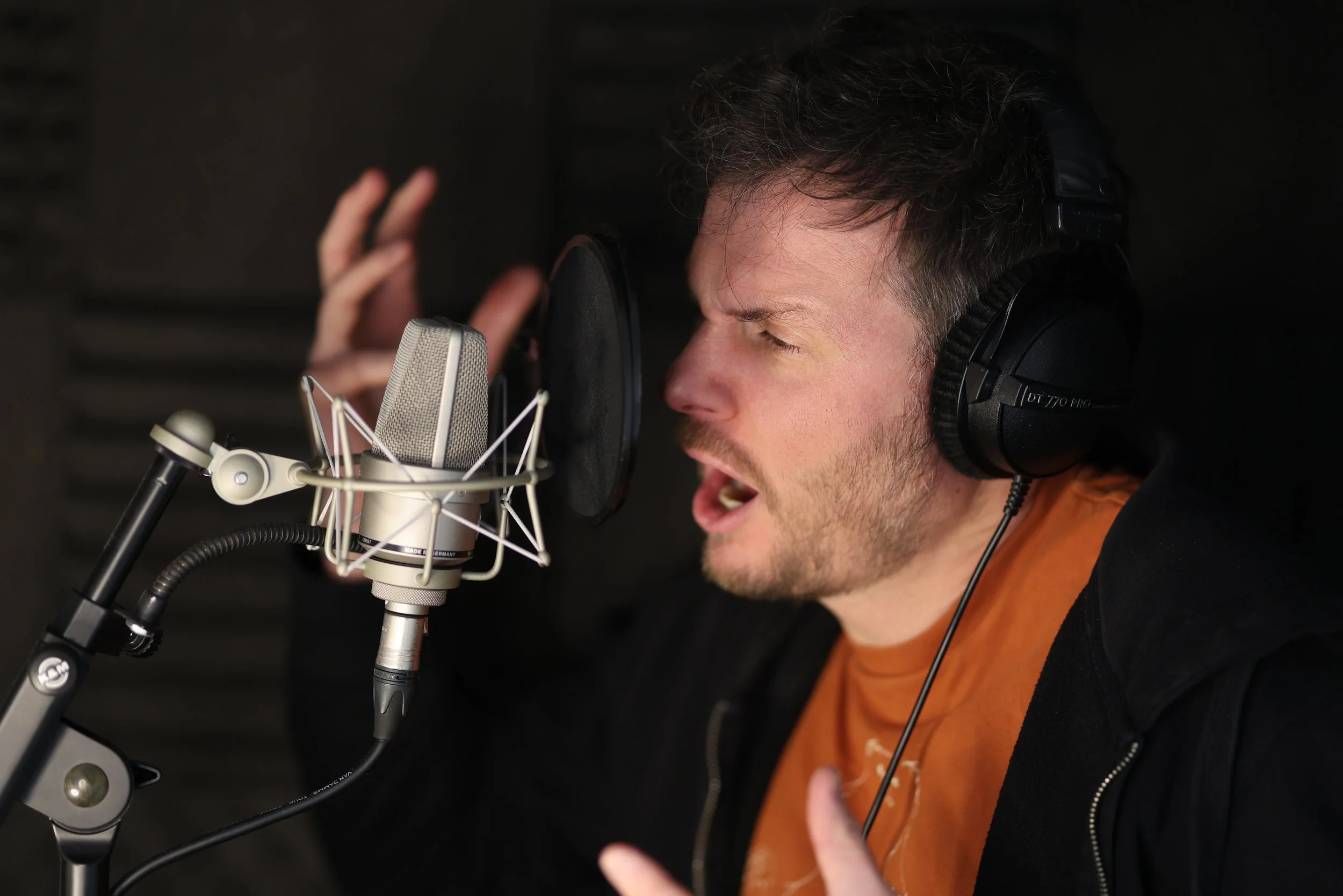 Man singing into a professional microphone in a recording studio wearing headphones
