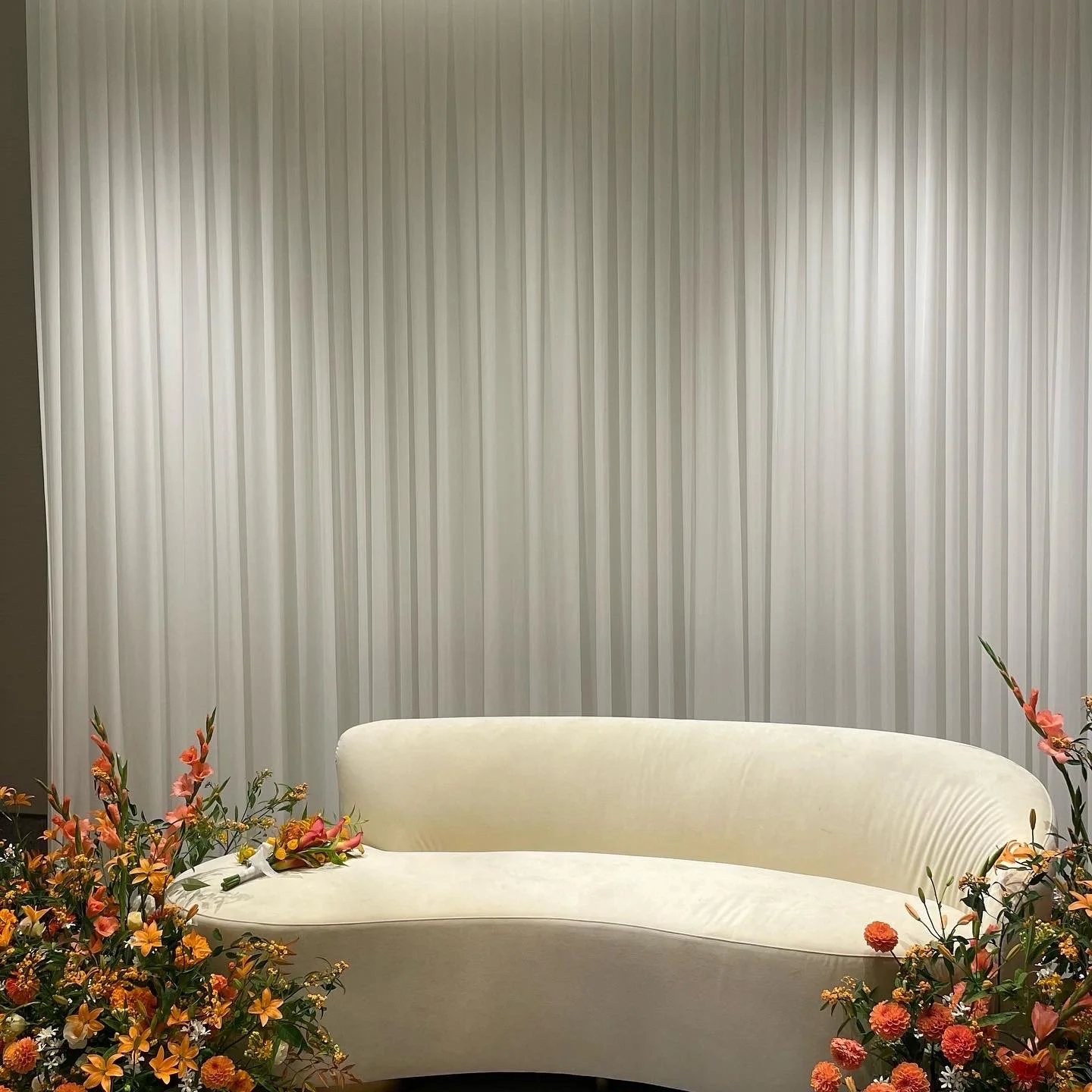 Cream-colored sofa with floral decorations around it, set against a gray, textured curtain backdrop.