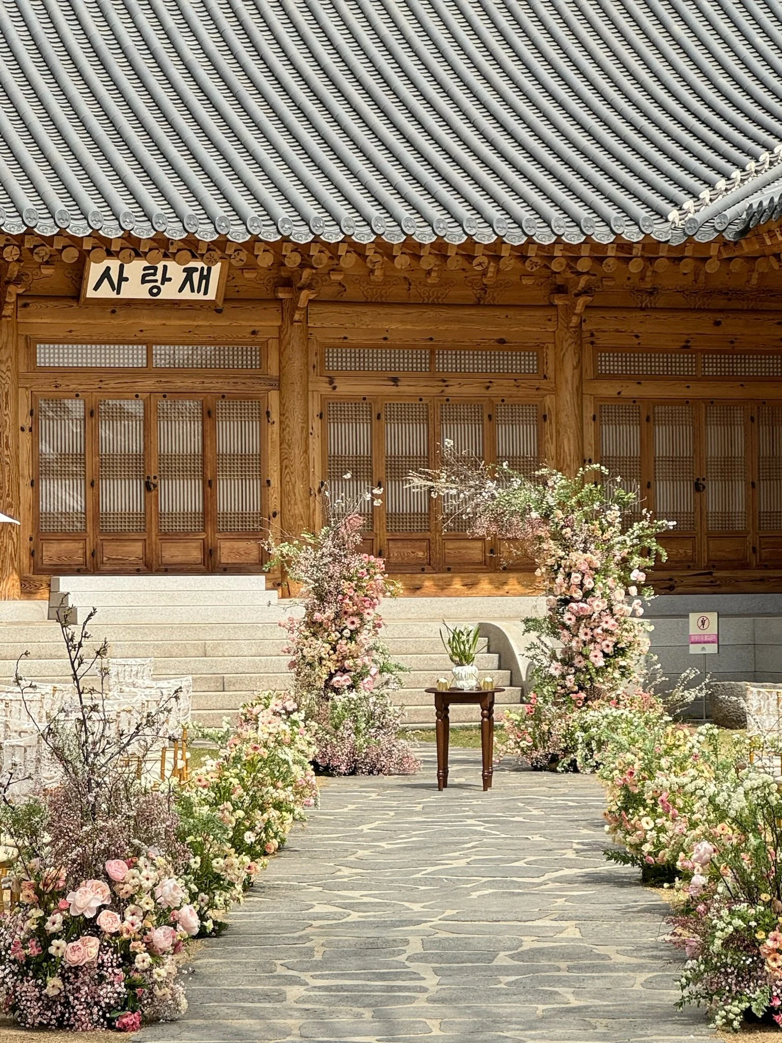Traditional Korean building with floral arrangements and a stone pathway leading to steps.