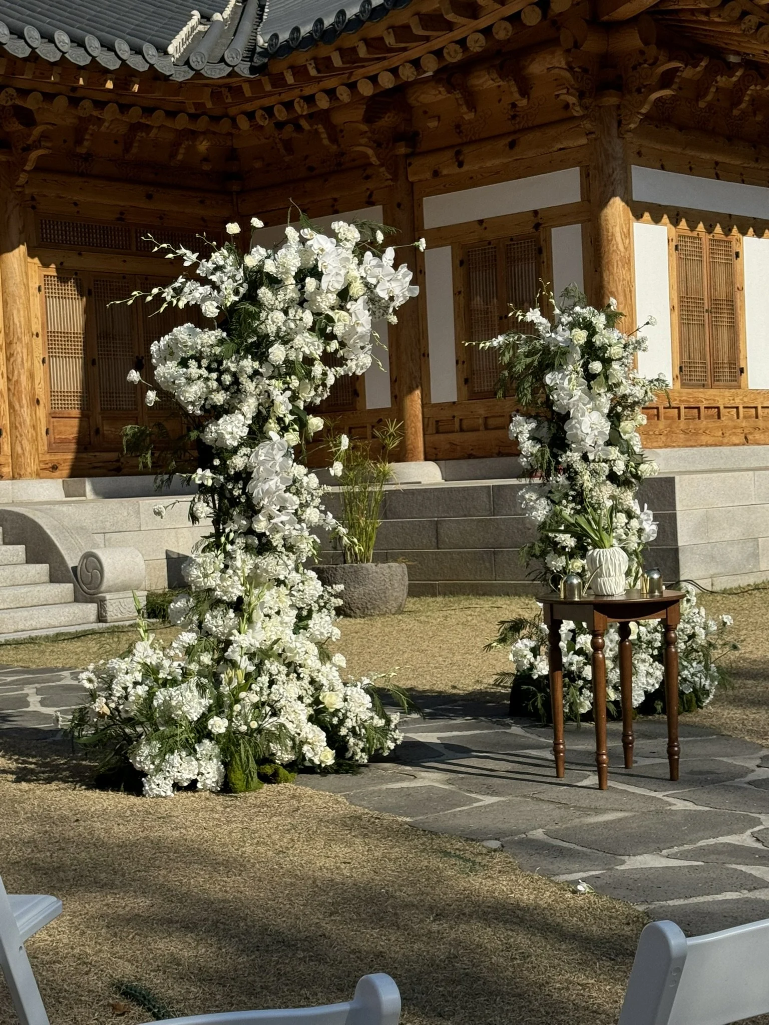 A wedding outdoor altar decorated with white flowers, with a traditional wooden building in the background.