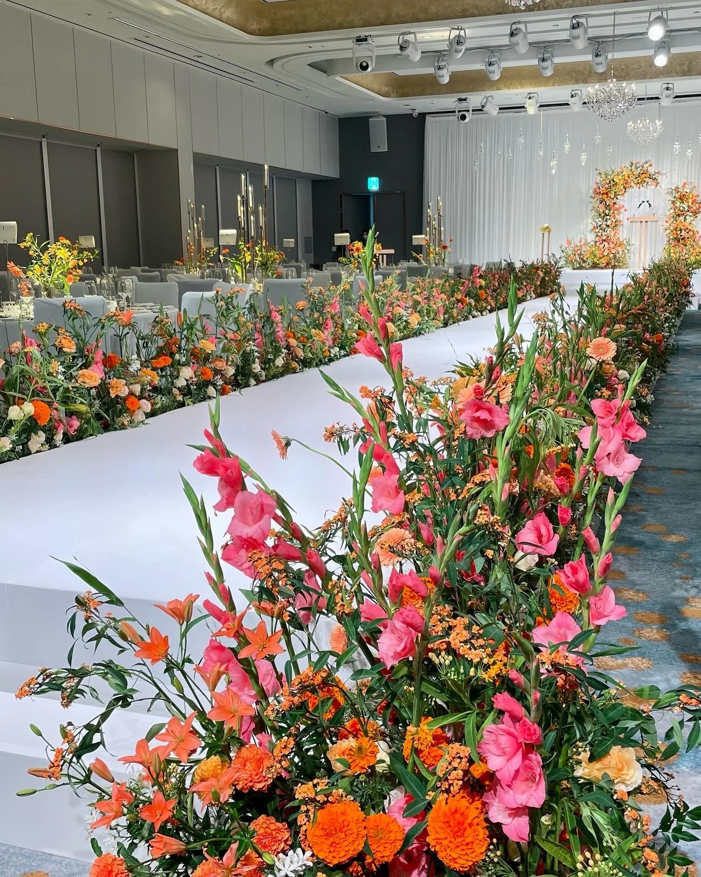 Indoor wedding venue with a long floral aisle, decorated with colorful flowers and candle holders, and an elegant stage at the end.