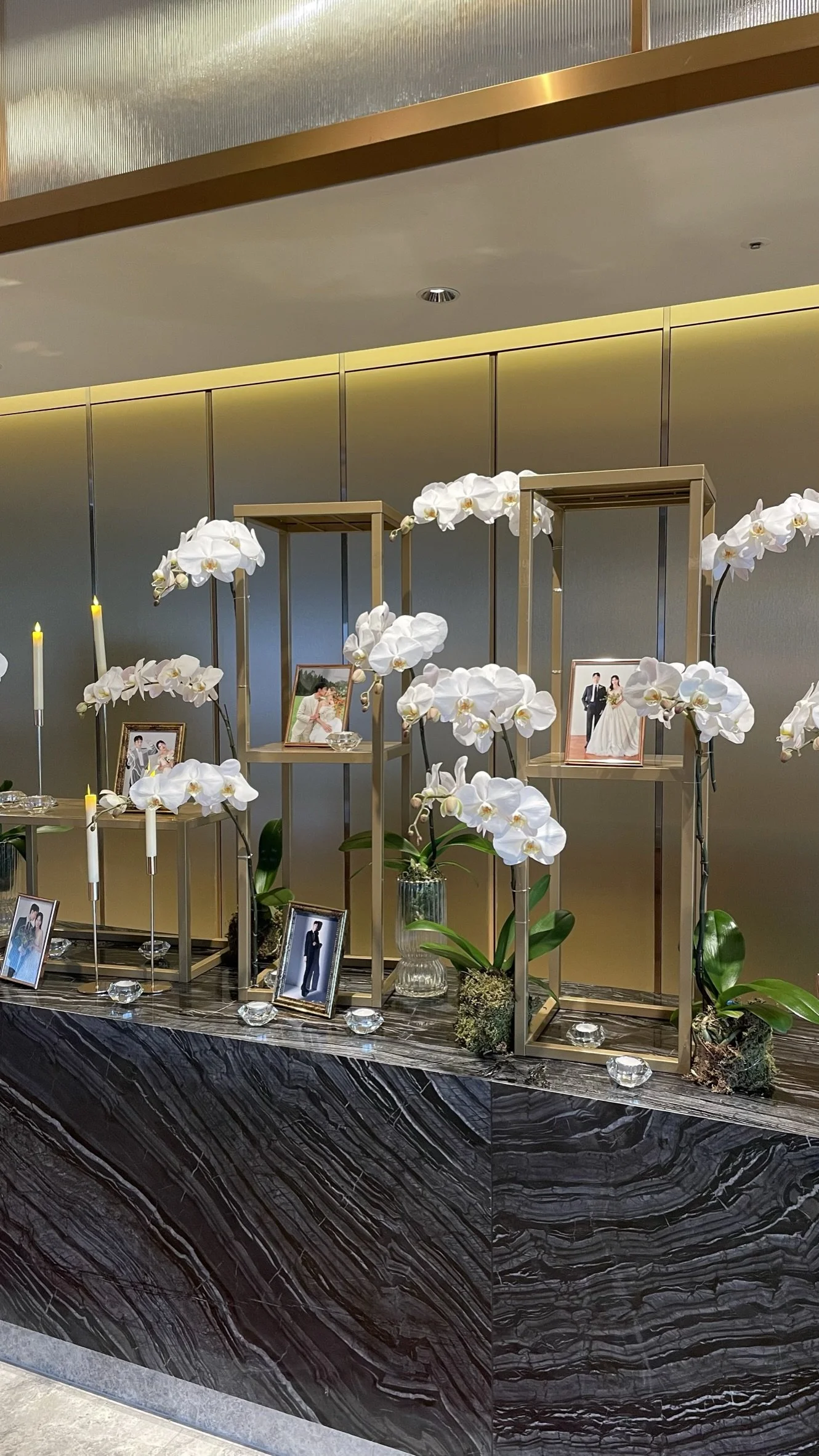 Decorative display with framed wedding photos, white orchids, and small candles on a marble counter.