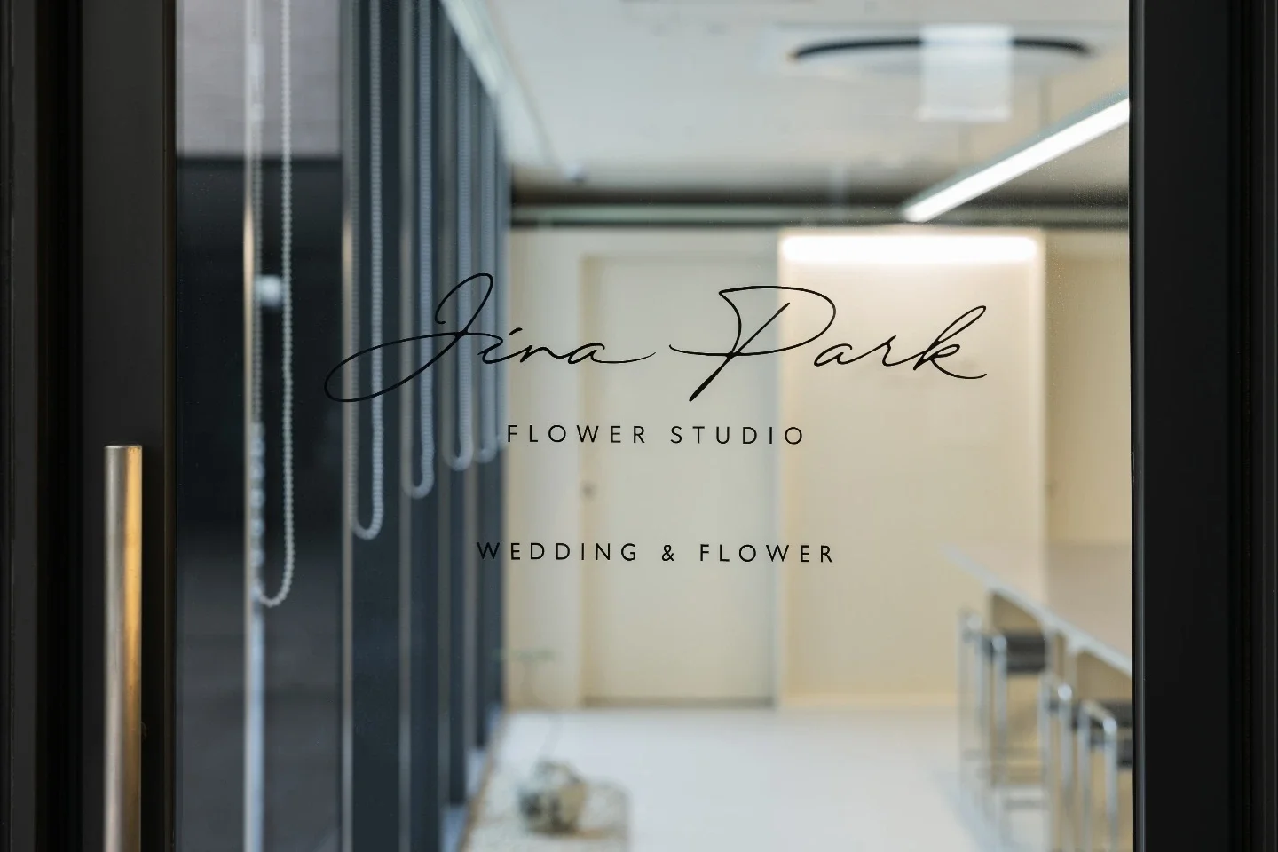 Glass door with the text 'Jina Park Flower Studio Wedding & Flower' in script and uppercase font, leading into a wedding and flower studio interior.