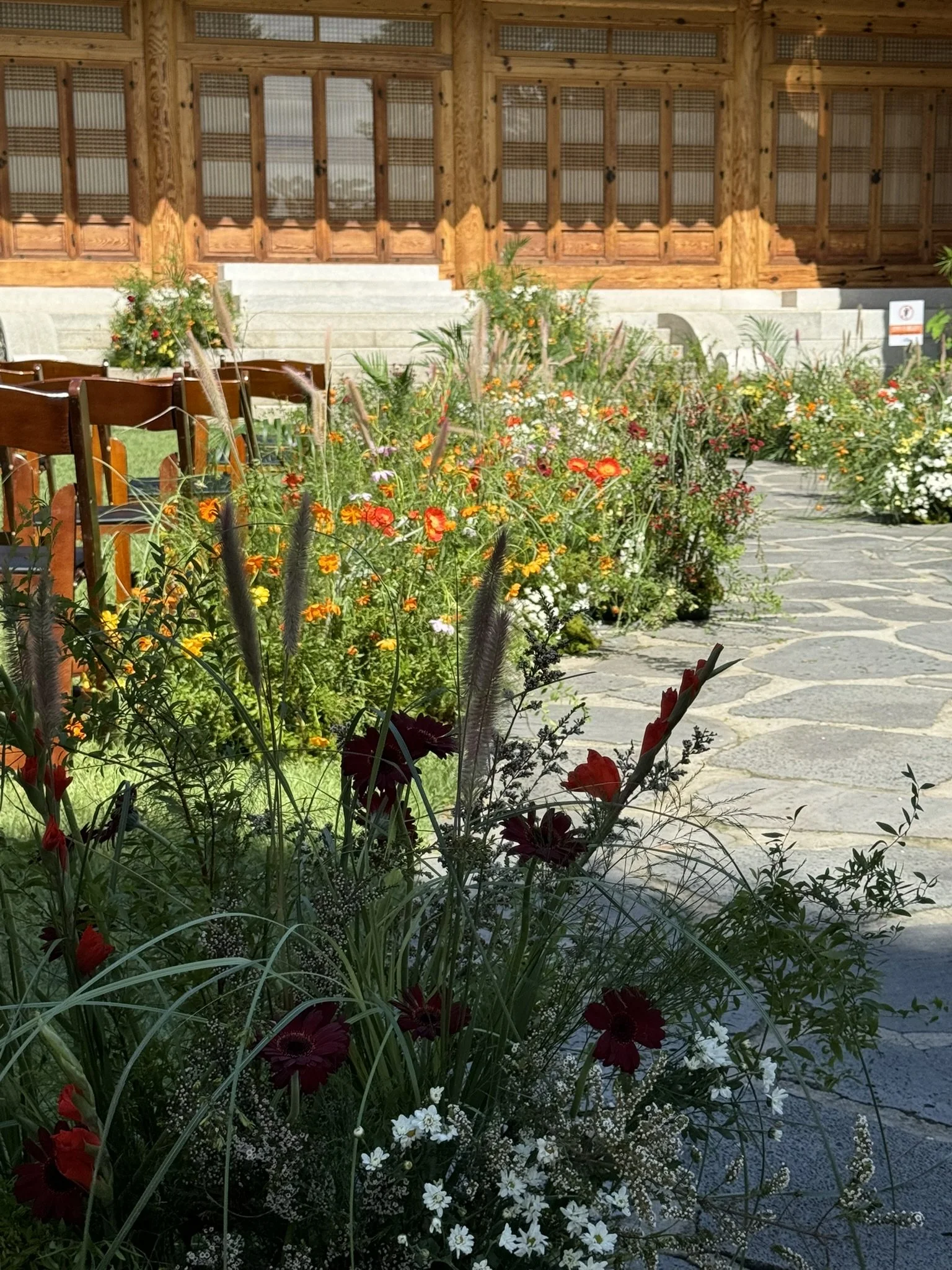 A garden with colorful flowers, stone pathway, and wooden building in the background.