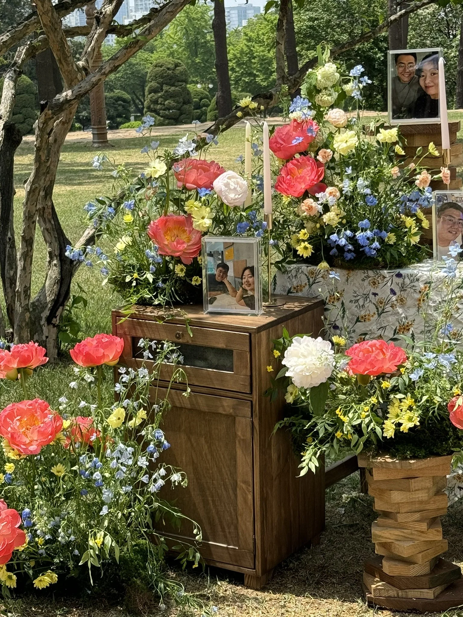 A memorial setup with colorful flowers, framed photos, and candles outdoors in a park.