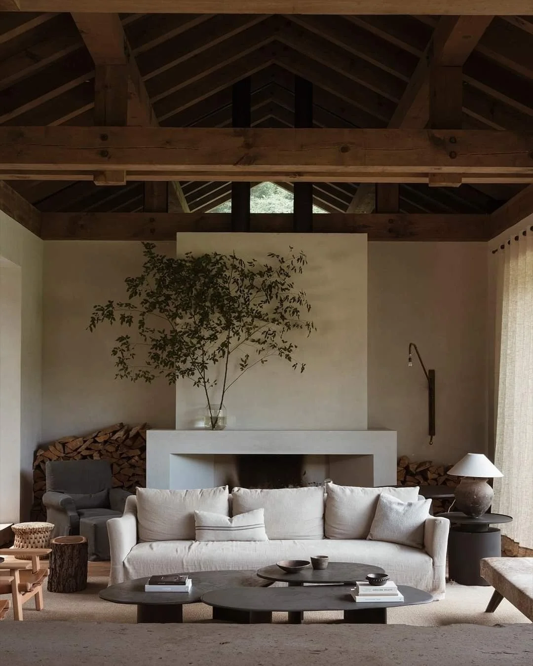 Woonkamer met ingebouwde haard en grote aardewerken vaas met boom in natuurlijke interieursetting.
