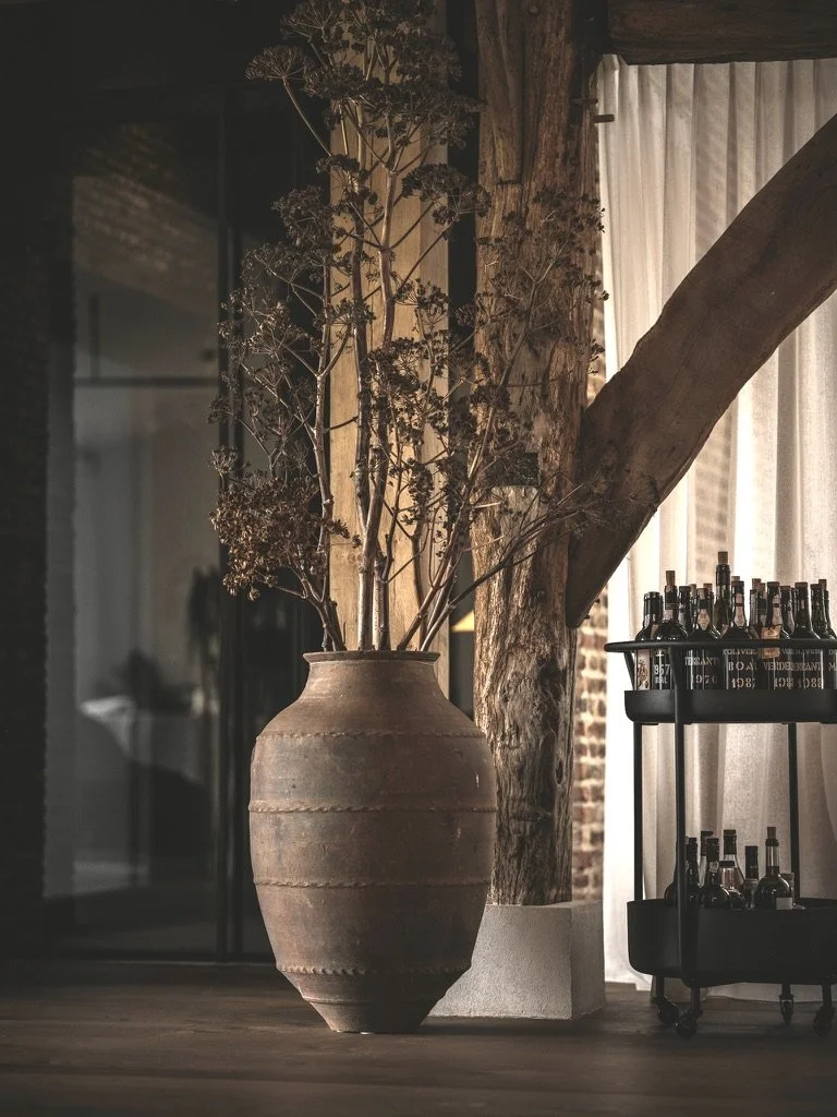 Een grote, antieke aardewerken vaas met gedroogde takken in een restaurant met drankwagen ernaast.