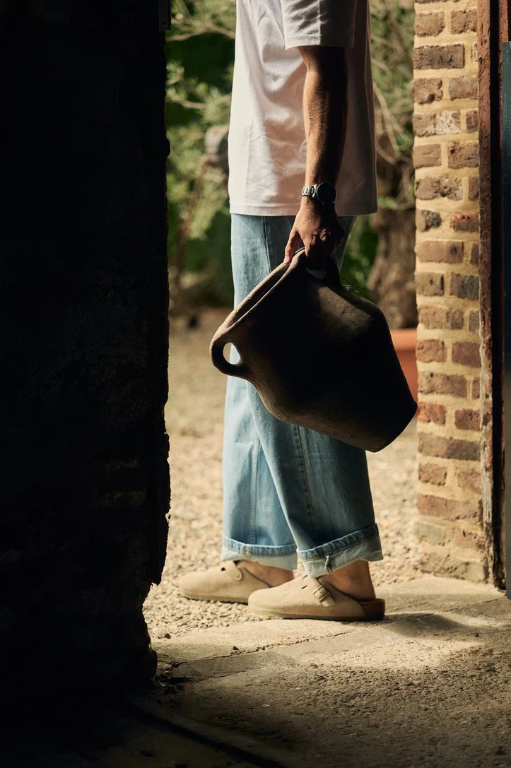 Grote aardewerken vaas in karaktervolle buitenruimte met bakstenen muur.