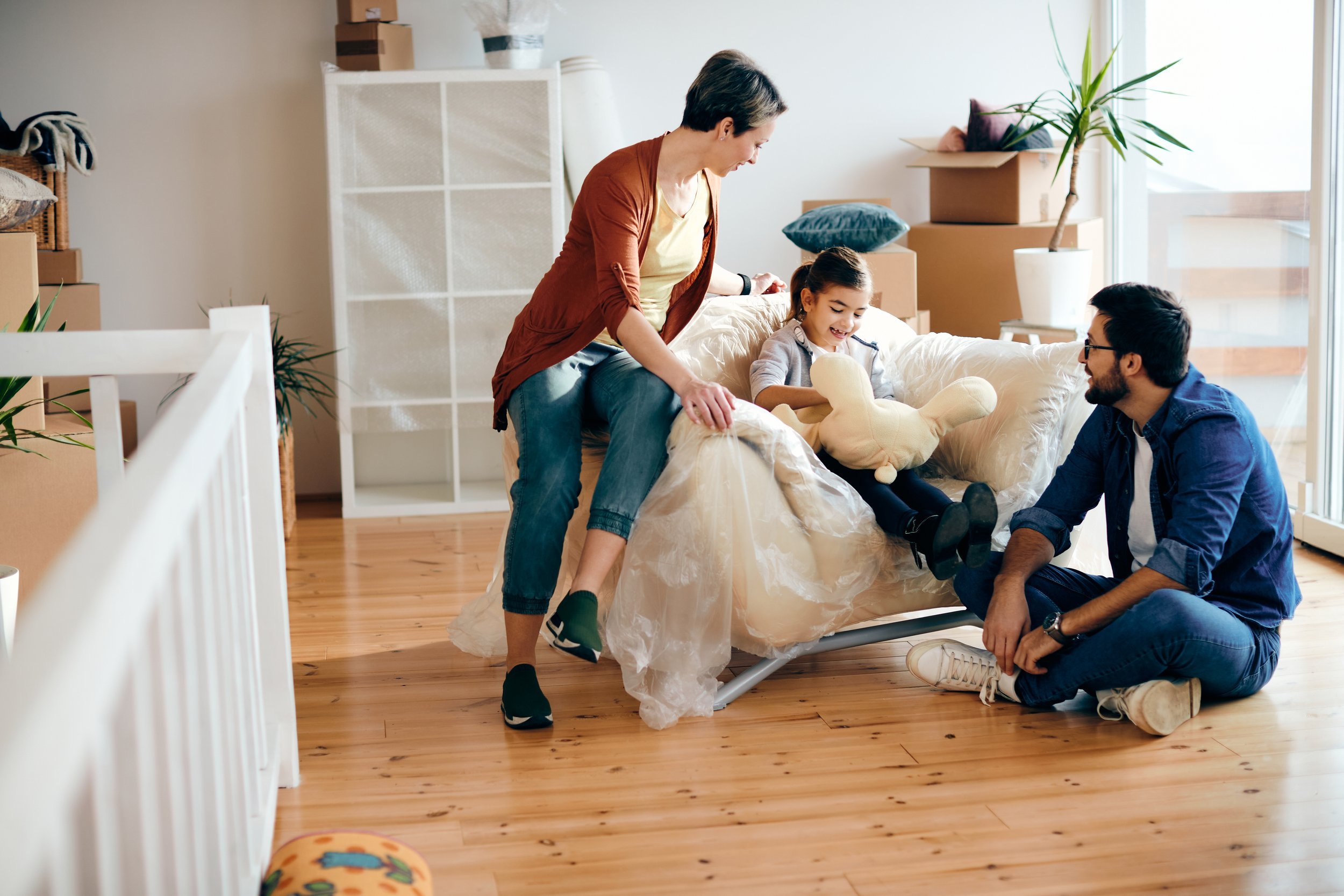 Parents and child sit together on a couch in a bright living room surrounded by moving boxes, sharing a relaxed moment that reflects rebuilding connection and emotional safety within a family.