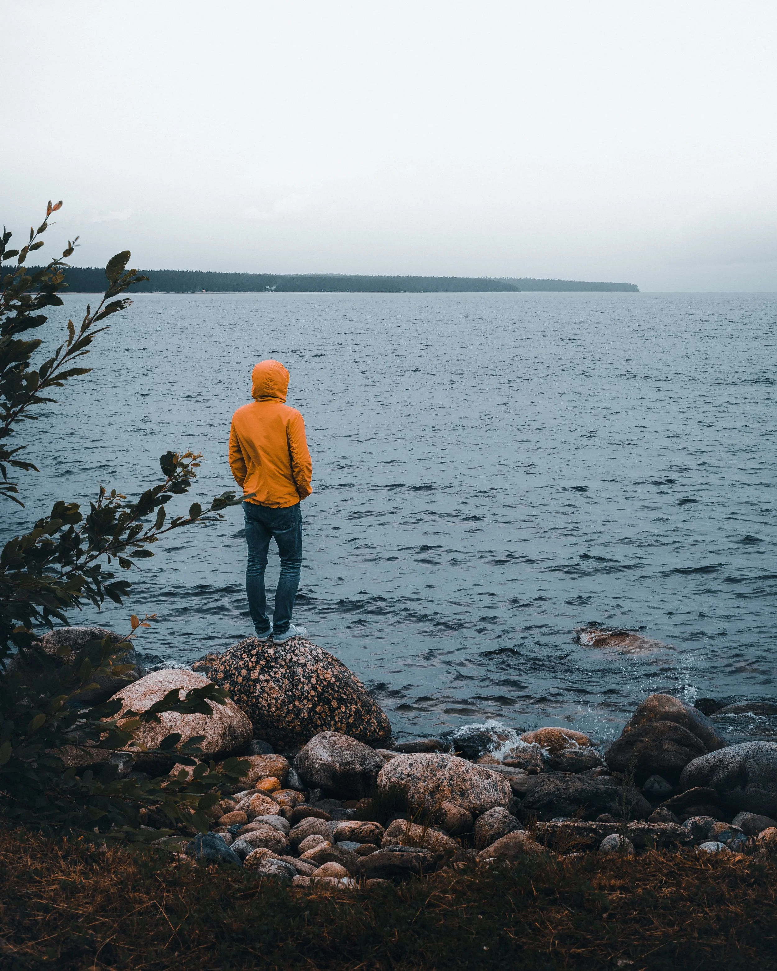 Woman standing alone on a rocky shoreline, reflecting on identity after relational trauma.