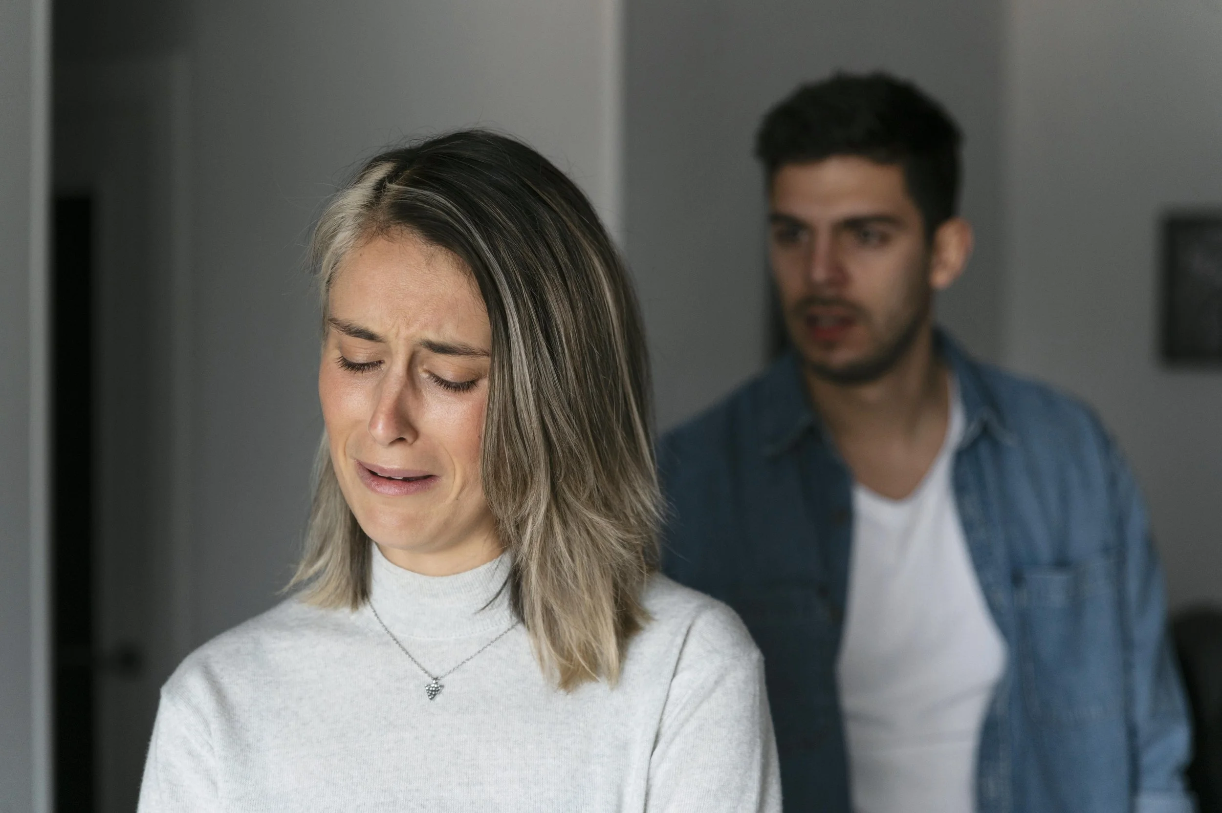 Crying woman in the foreground with her partner blurred behind her, representing the healing process from sexual trauma