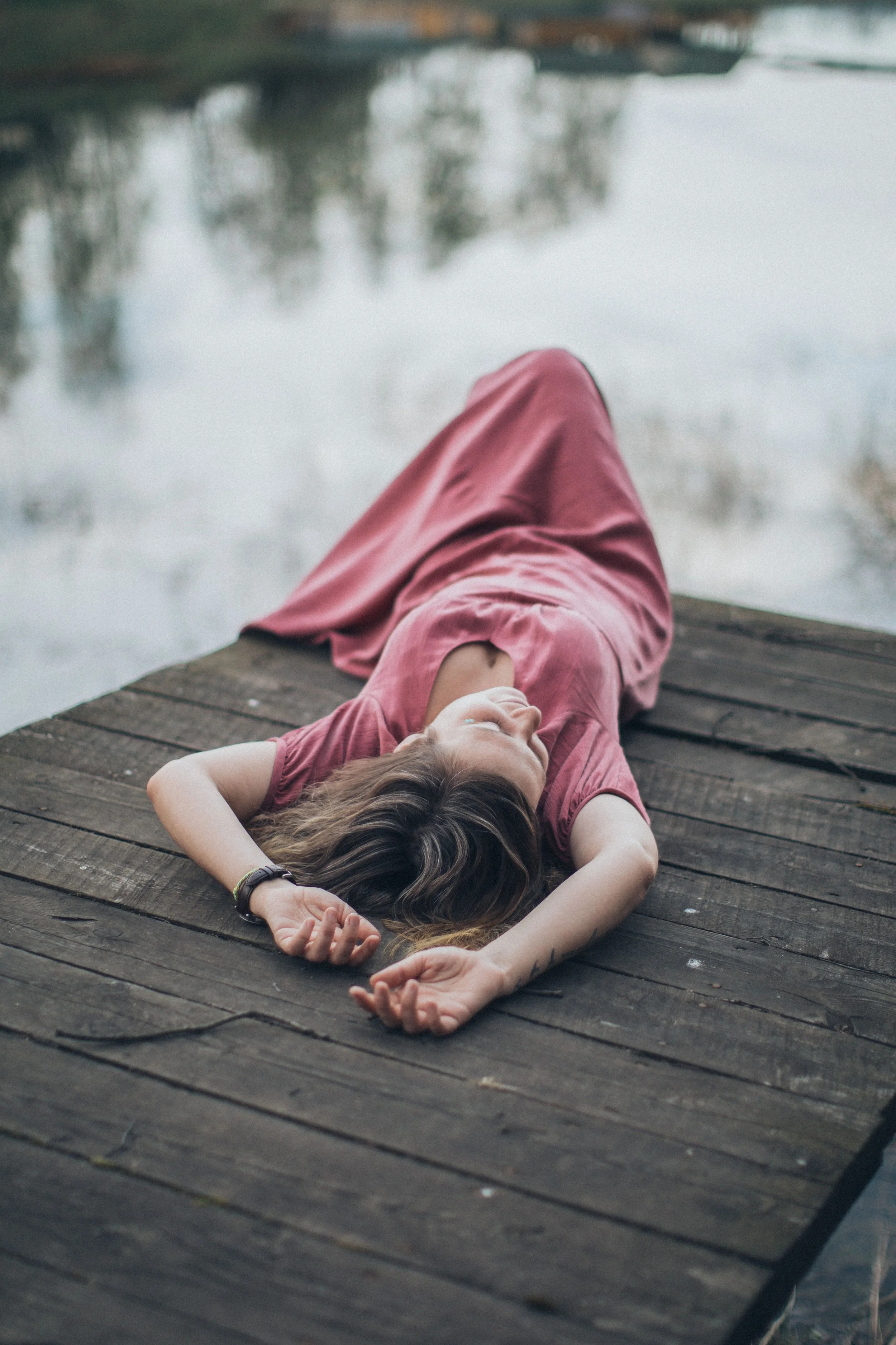 Woman resting on a dock by the water, representing emotional overwhelm, trauma recovery, nervous system healing, and the challenges of healing after trauma.