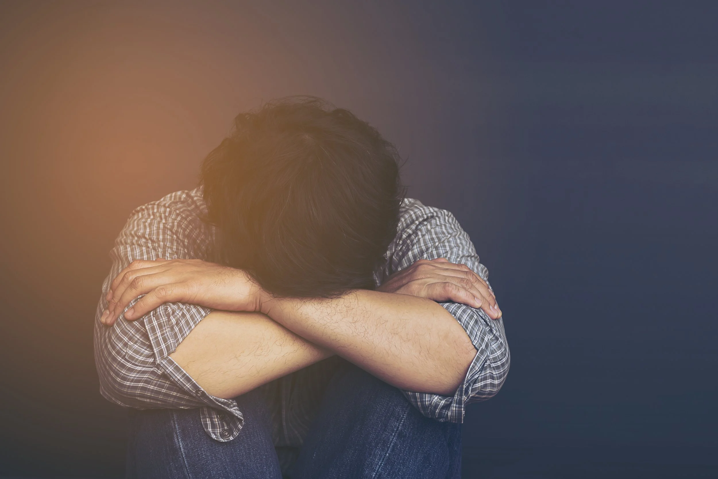Man sitting with his head down on his knees and arms wrapped around them, depicting emotional dysregulation from trauma