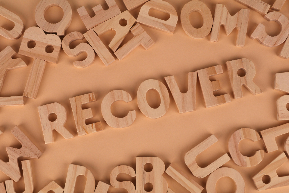Wooden letters scattered on a neutral background spelling “recover” to represent healing and rebuilding self worth after abuse.