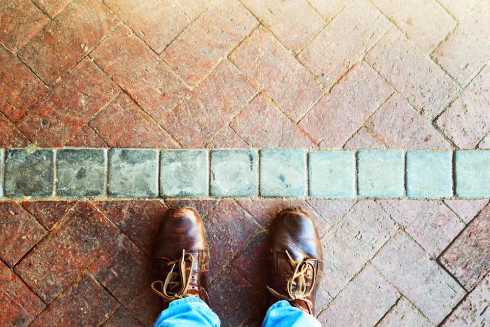 Person wearing brown shoes standing at a line between two different brick patterns on the ground, symbolizing setting personal boundaries.