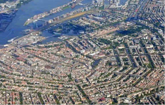 Luchtfoto van Amsterdam met een rivier, bruggen, veel gebouwen en groenstroken.