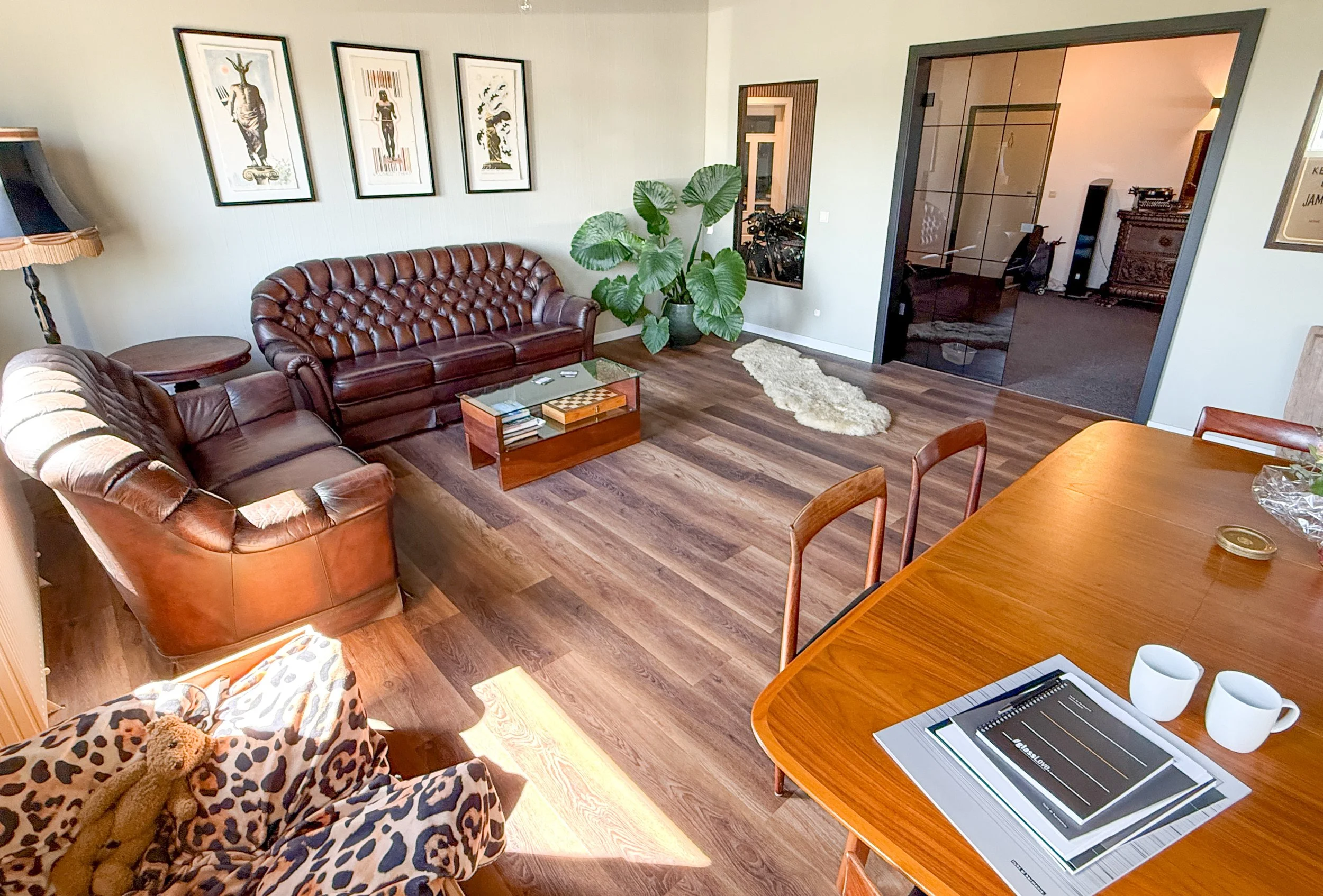Loungebereich der Firma Prompt. Man sieht eine Chesterfield Ledercouchgarnitur, Bilder die an der Wand hängen und eine doppelflüglige Lofttür aus dunklem Glas.