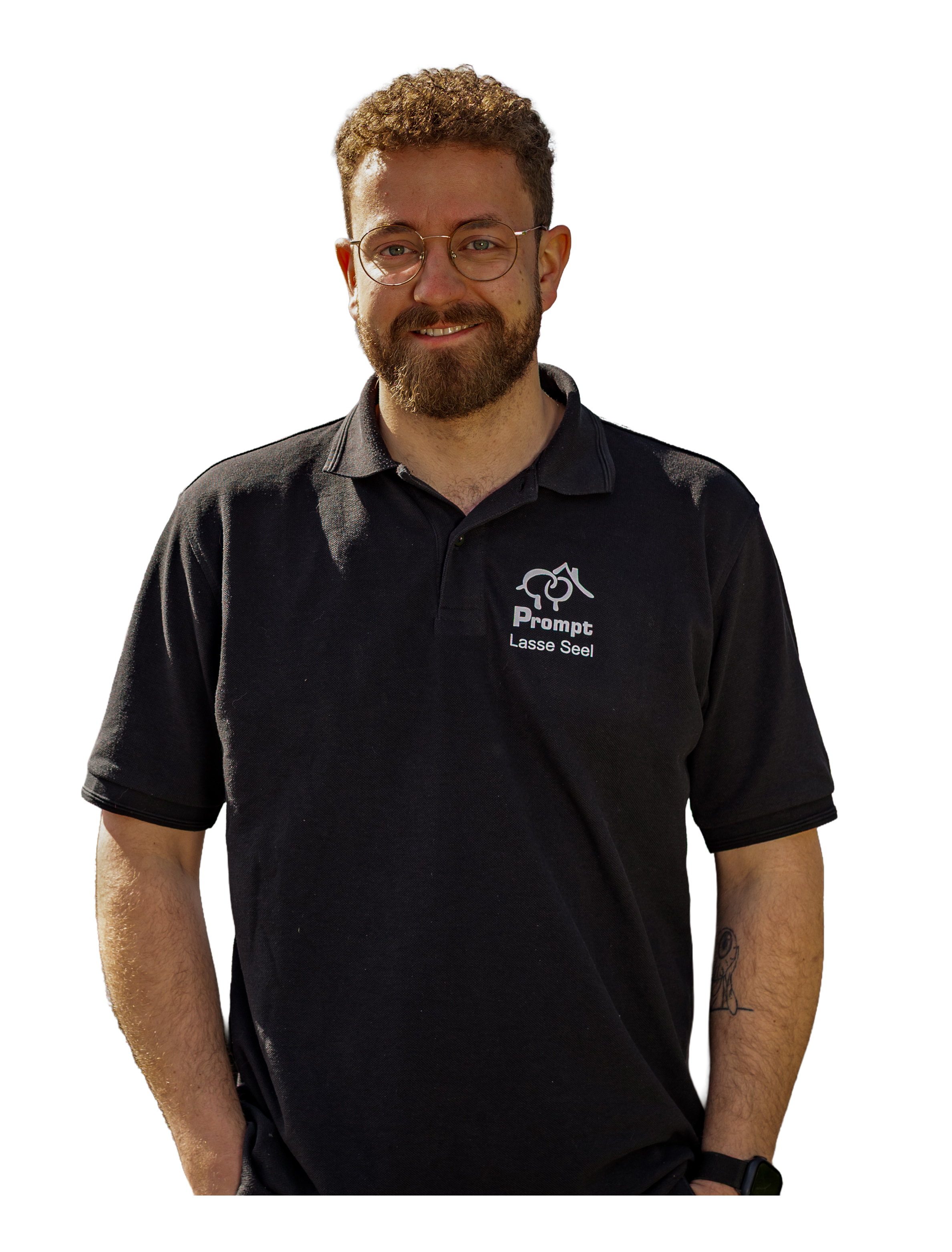 Ein junger Mann trägt eine schwarze Polo-Hemd mit Logo und Text, trägt eine Brille, hat einen Bart und Tattoos am Arm, lächelt leicht, steht vor einem dunklen Hintergrund.