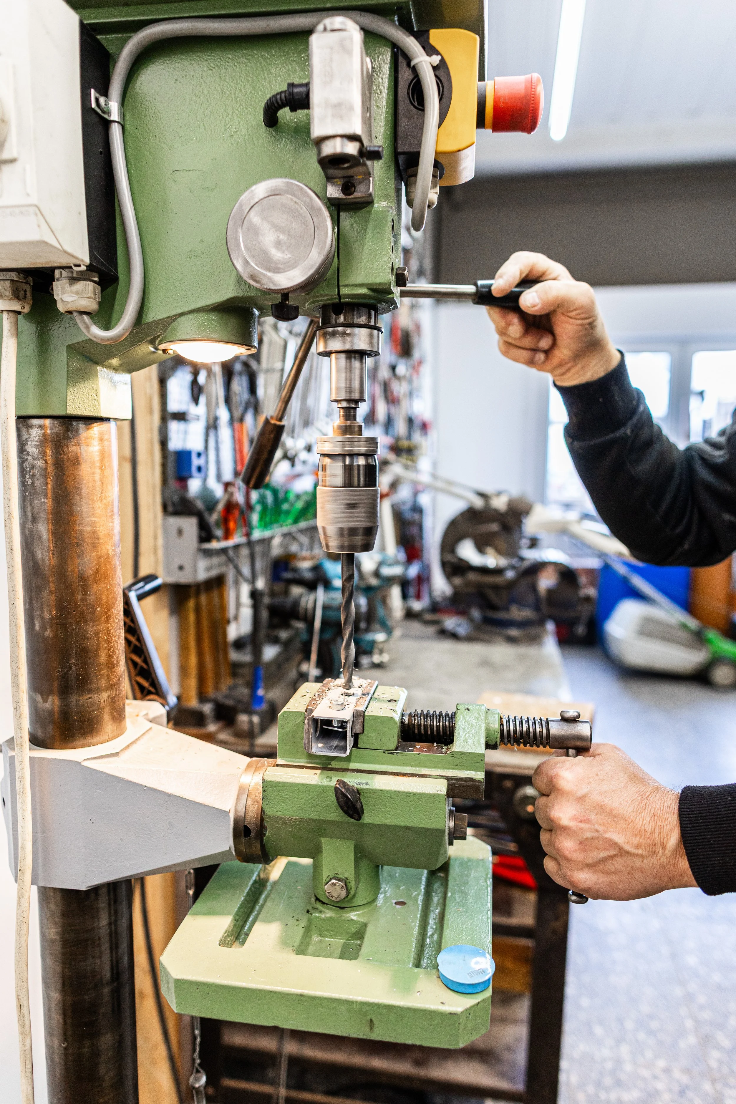 Person bedient eine Standbohrmaschiene in einer Werkstatt.