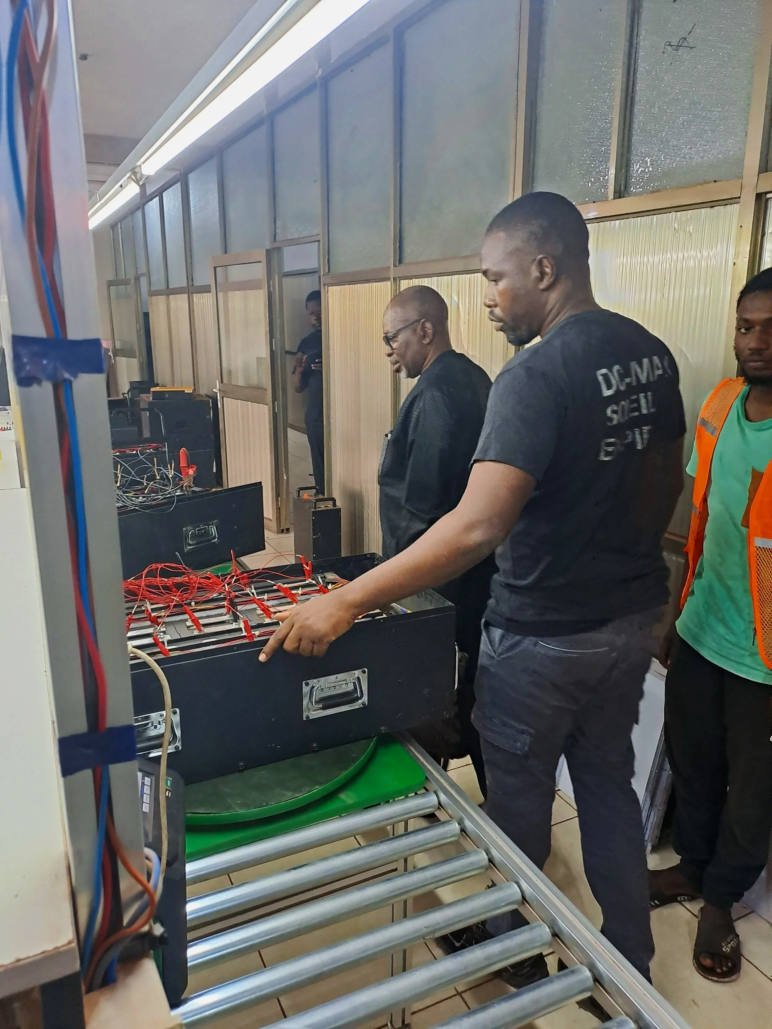 Three men working with electronic equipment and wires on a worktable in a laboratory or workshop.