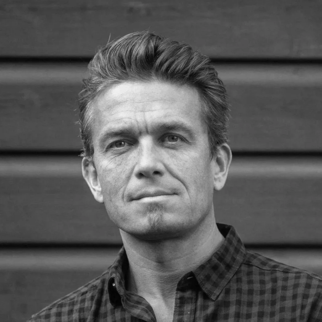 Black and white portrait of a man with short, styled hair wearing a checkered button-up shirt, looking slightly to the side with a serious expression.