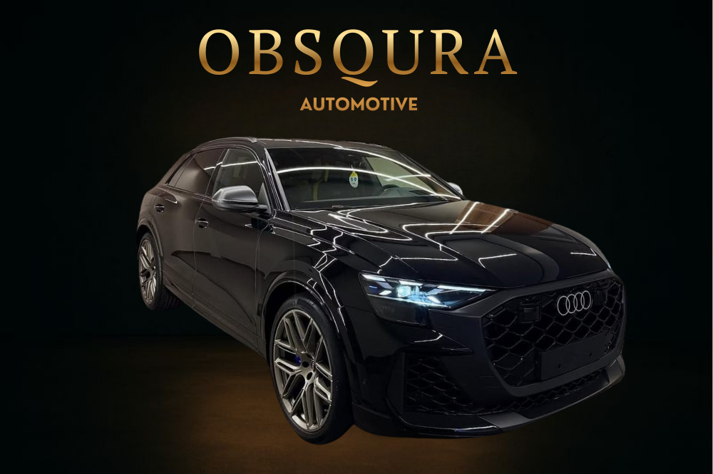 A black Audi SUV in a dark showroom with the words "Obscura Automotive" in gold lettering above it.