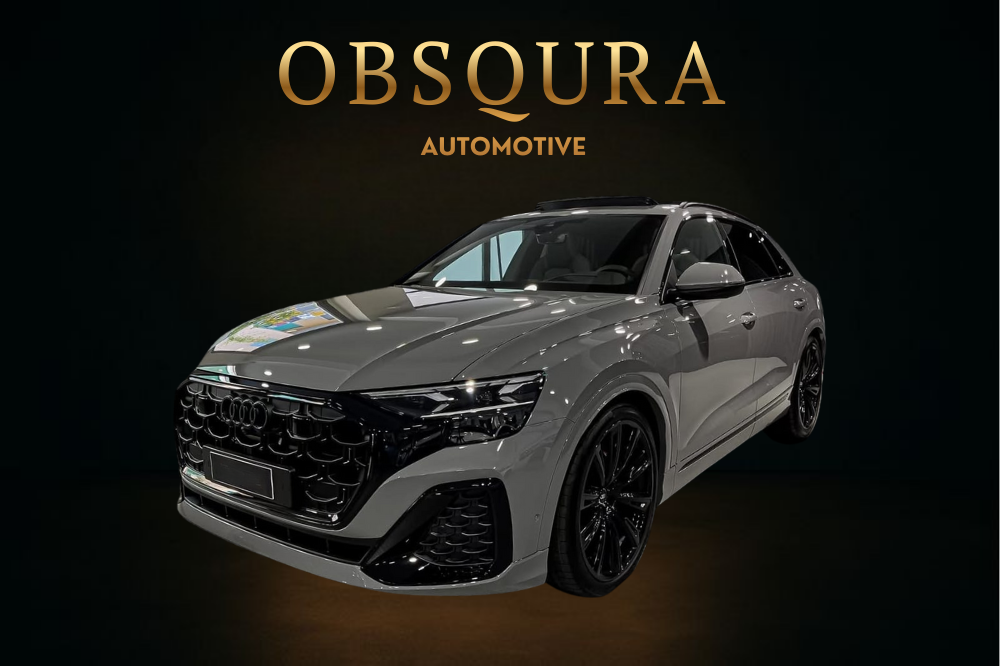A sleek, gray Audi SUV showcased in a dark setting with the word 'OBSCURA' in large gold letters and 'AUTOMOTIVE' below it, indicating a car dealership or brand presentation.