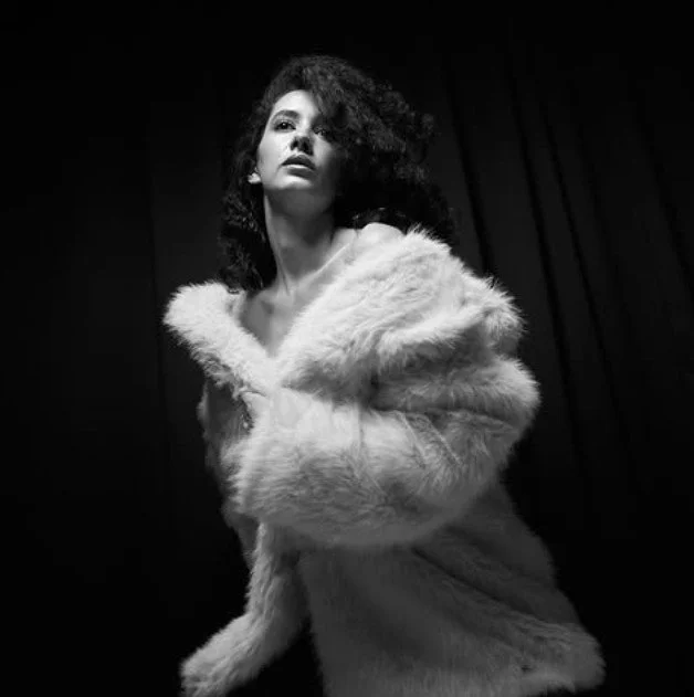 Schwarz-weiß-Foto eines jungen Models in einer weichen Felljacke vor dunklem Hintergrund.