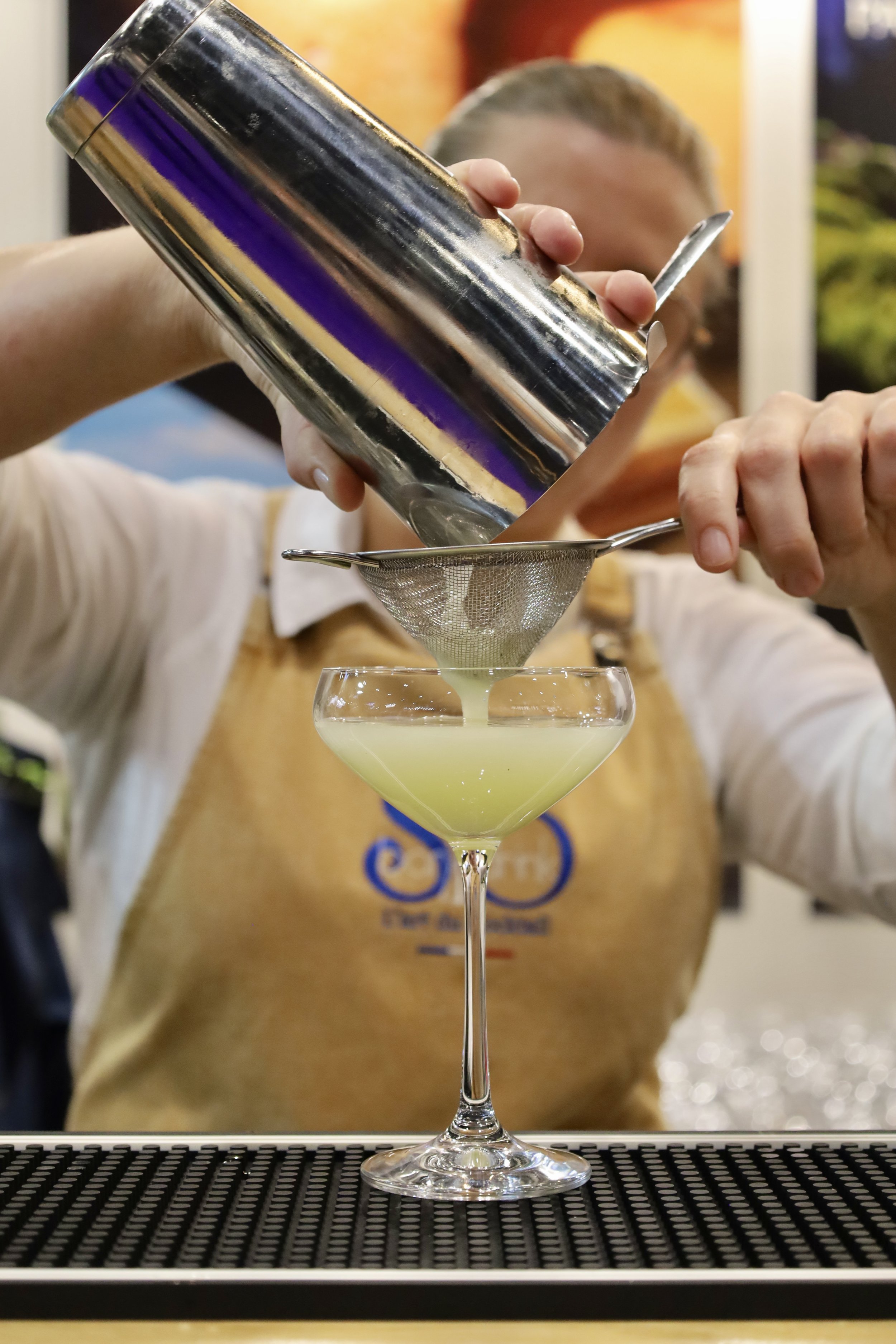 Un barman verse un cocktail vert clair à travers un tamis dans un verre à cocktail.