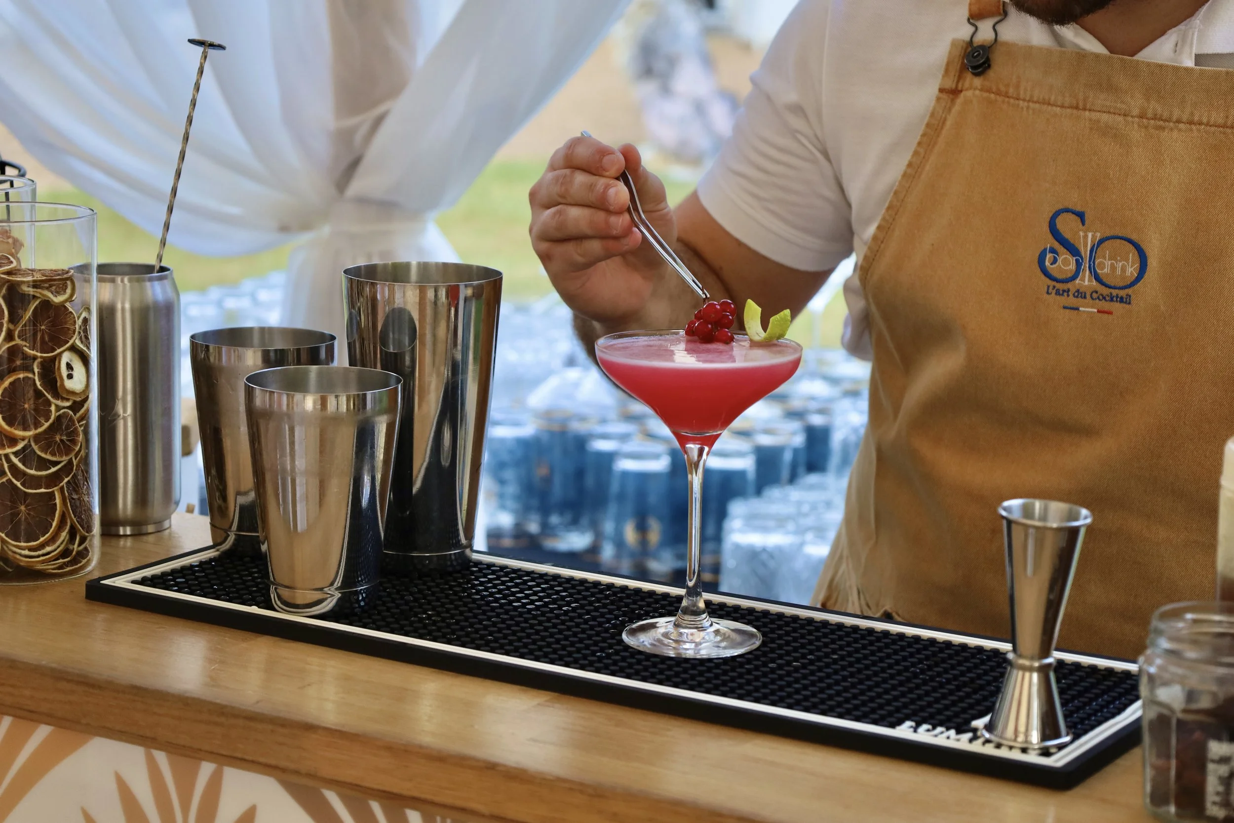 Une personne en train de garnir un cocktail Rose dans un verre à martini avec des groseilles rouges et un zeste de citron.